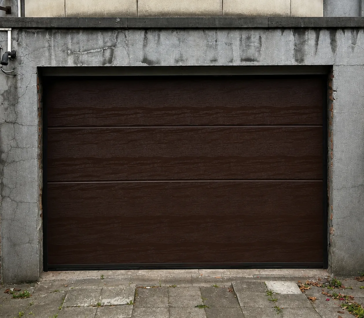Porte de garage en bois foncé encadrée par un mur en béton gris fissuré.