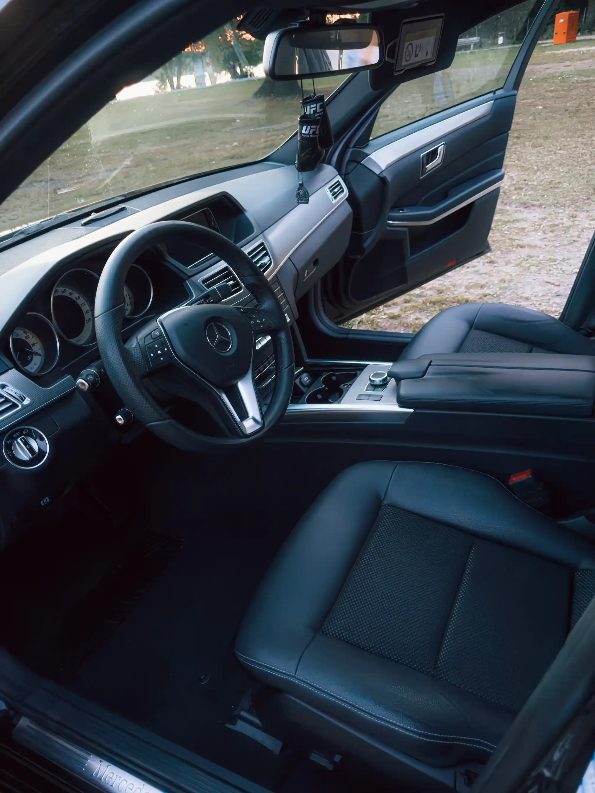 Interior view of a Mercedes car showing the steering wheel, driver seat, and open front passenger door.