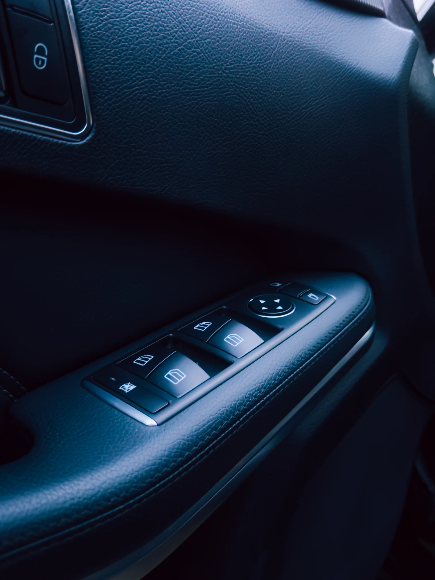 Close-up of car door panel with window control and mirror adjustment buttons in black leather interior.
