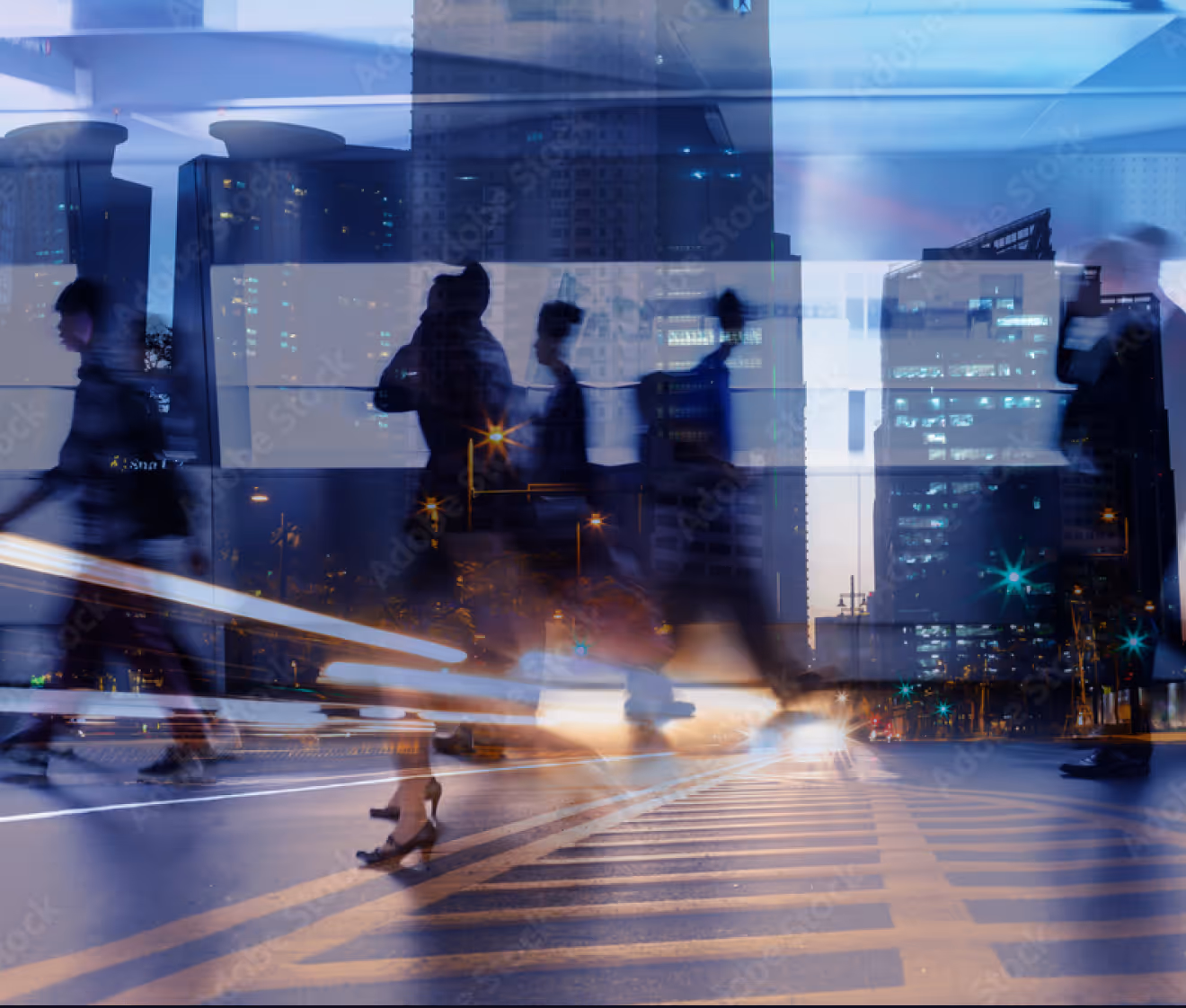 Blurred people walking on a city street at night with illuminated buildings and light trails.