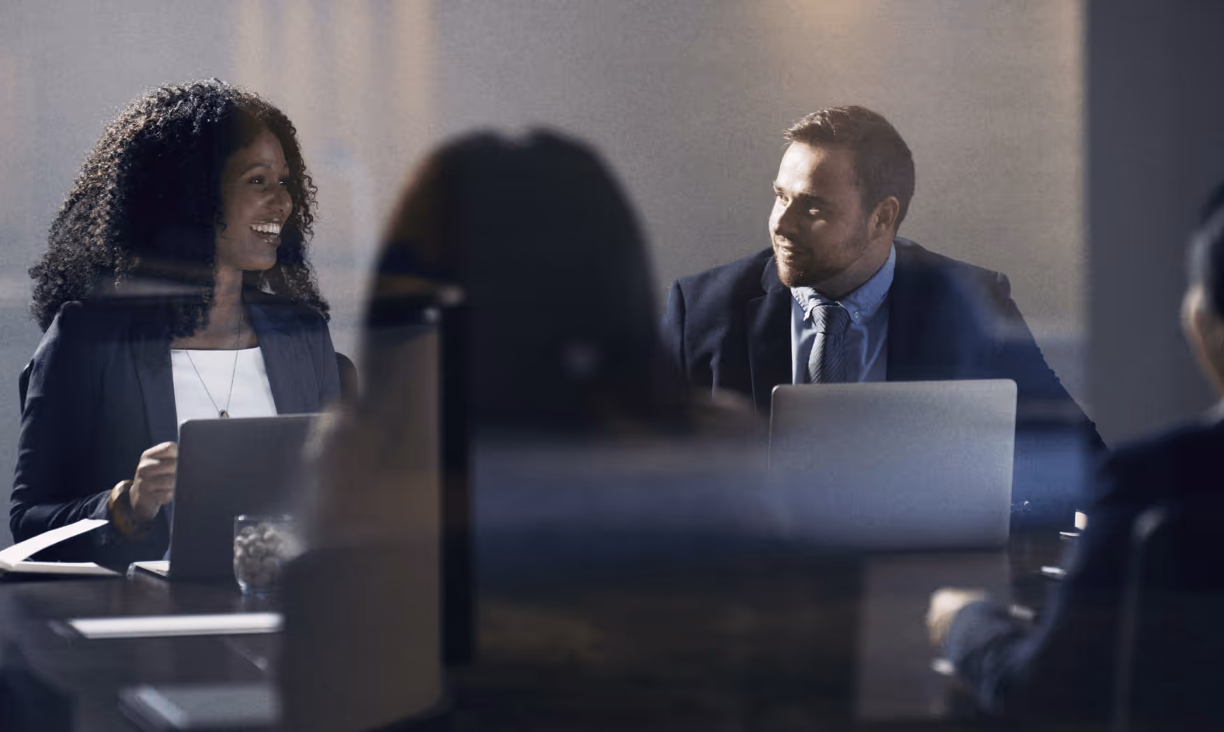 Two businesspeople smiling at each other during a meeting with laptops in front of them.