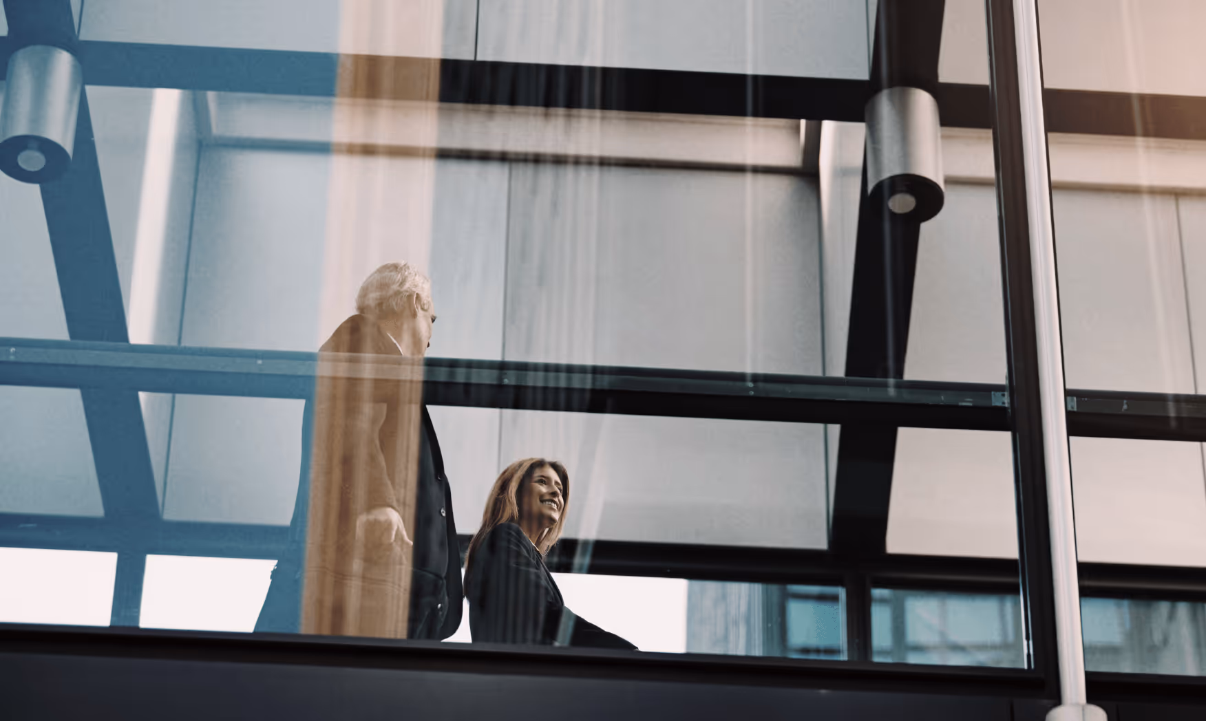 Businessman and businesswoman walking together in a modern glass building corridor.