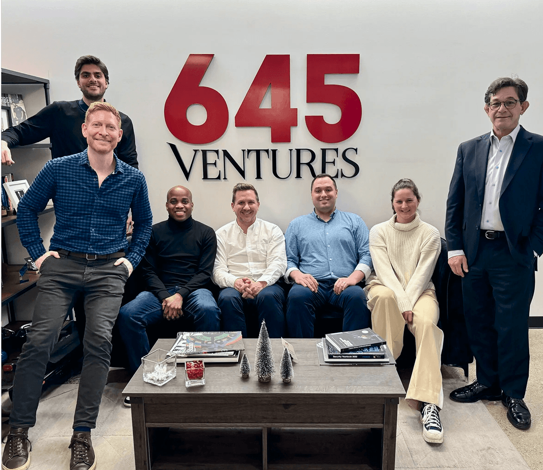Foresight team posing together in front of a "645 Ventures" sign in an office lounge.


