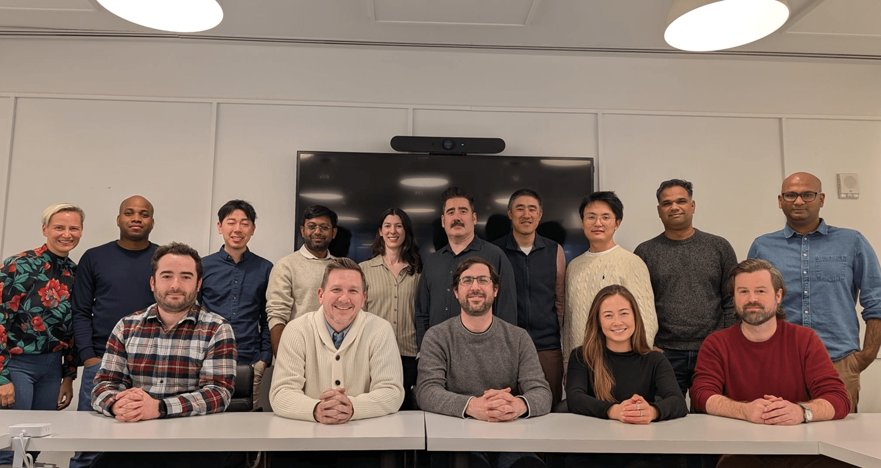 Full Foresight team group photo, colleagues posed in two rows in a conference room in front of a large wall-mounted display.