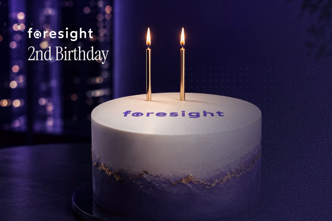 A white birthday cake with the Foresight logo and two lit candles, with "Foresight 2nd Birthday" text alongside.

