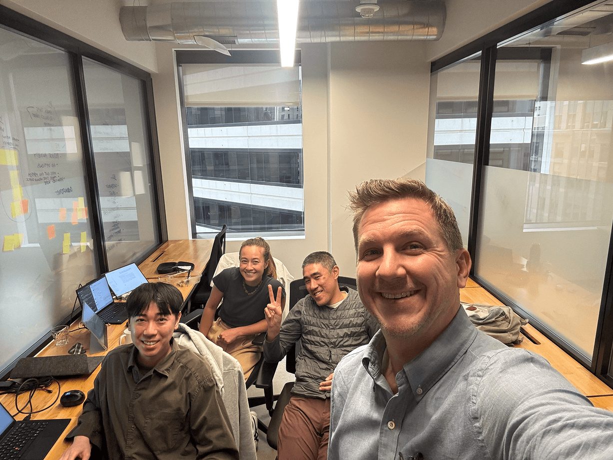 Foresight team members taking a playful selfie at their desks in a bright office with floor-to-ceiling windows and city views.