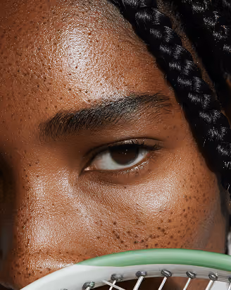 Close-up of a face with braided hair and a tennis racquet partially covering the mouth.