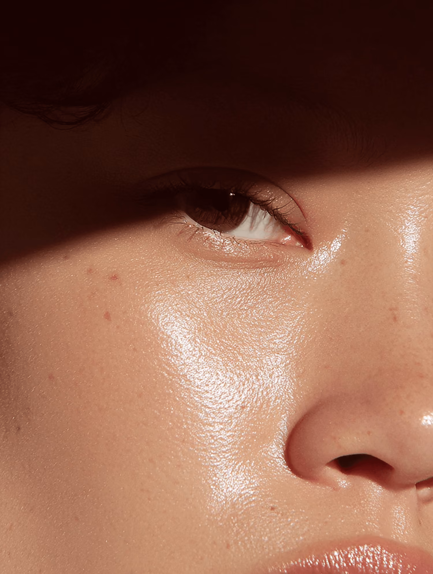 Close-up of a person’s glowing skin around eye, nose, and cheek with natural light and shadow.