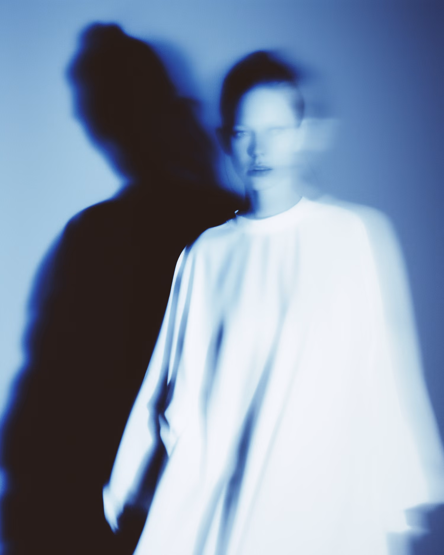 Blurred person in white clothing with a dark shadow on a blue background.