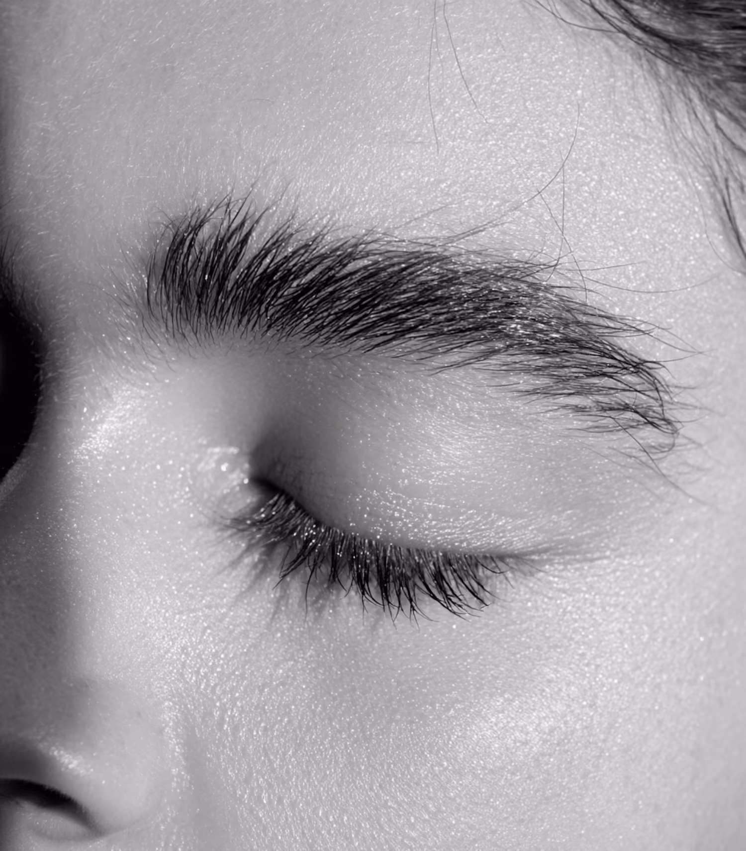 Close-up black and white photo of a person's closed eye with long eyelashes and thick eyebrow.