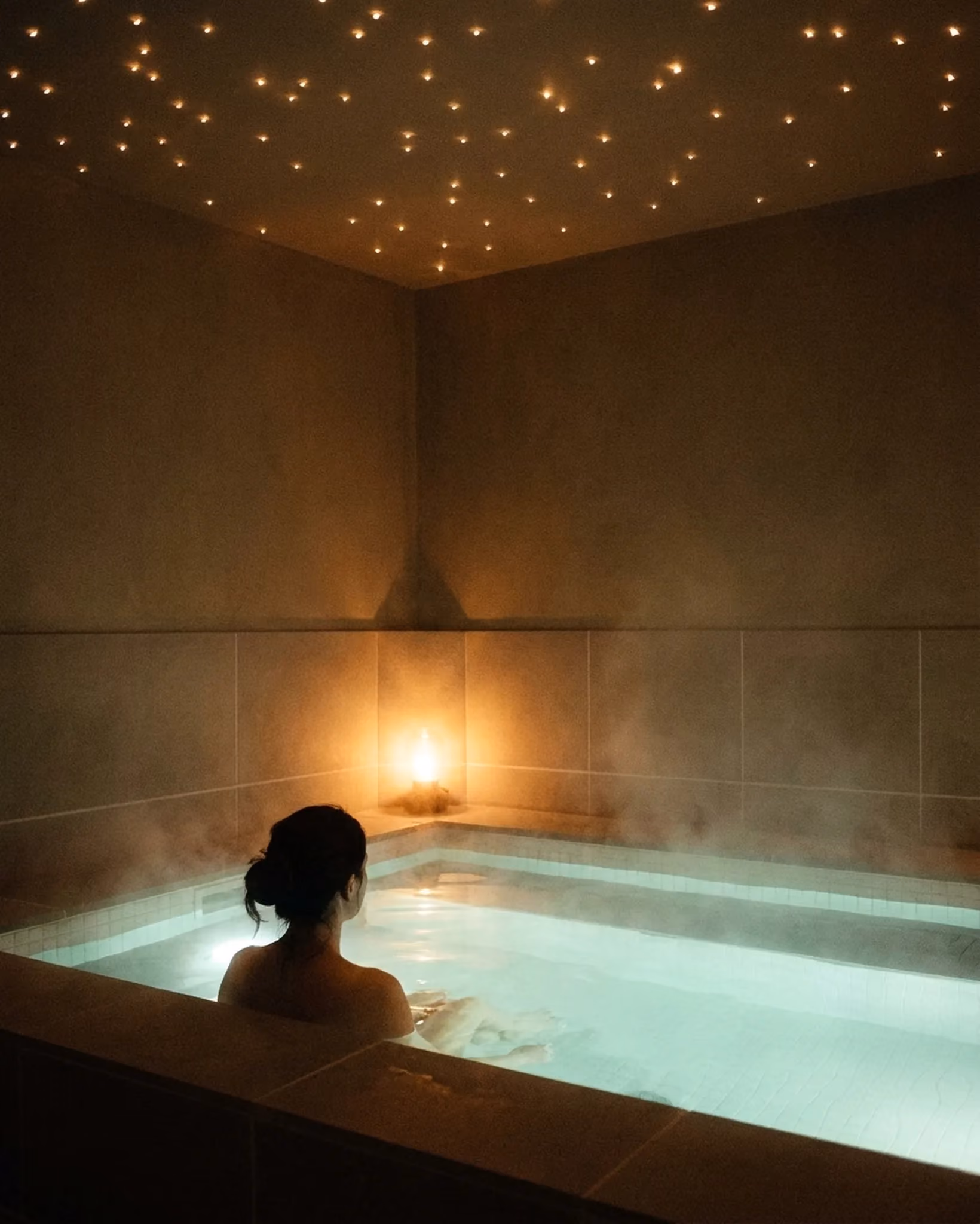 A guest floating in a warm, softly lit magnesium float pool at VELA
