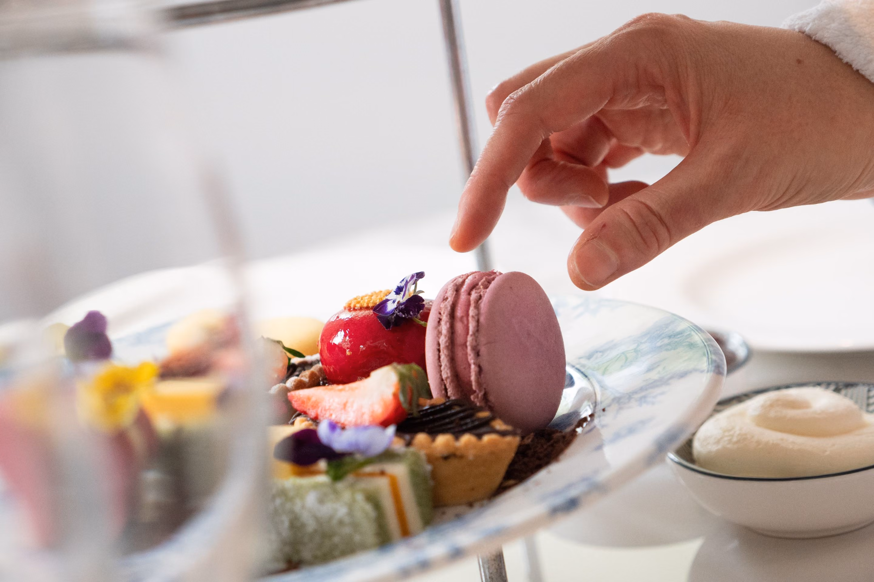 A guest choosing from a high tea plate of pastries and macarons at VELA