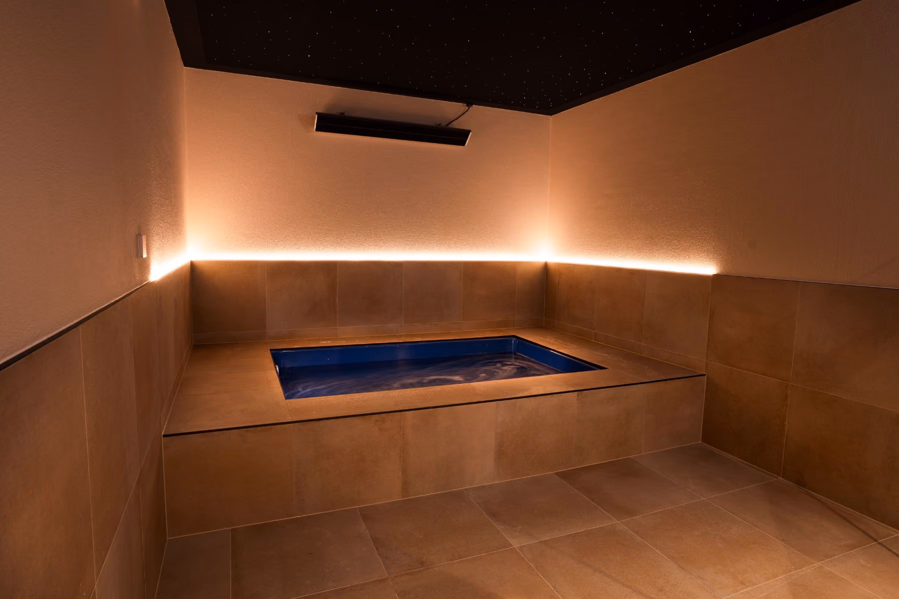 An empty open float pool at VELA, lit turquoise in a darkened private suite