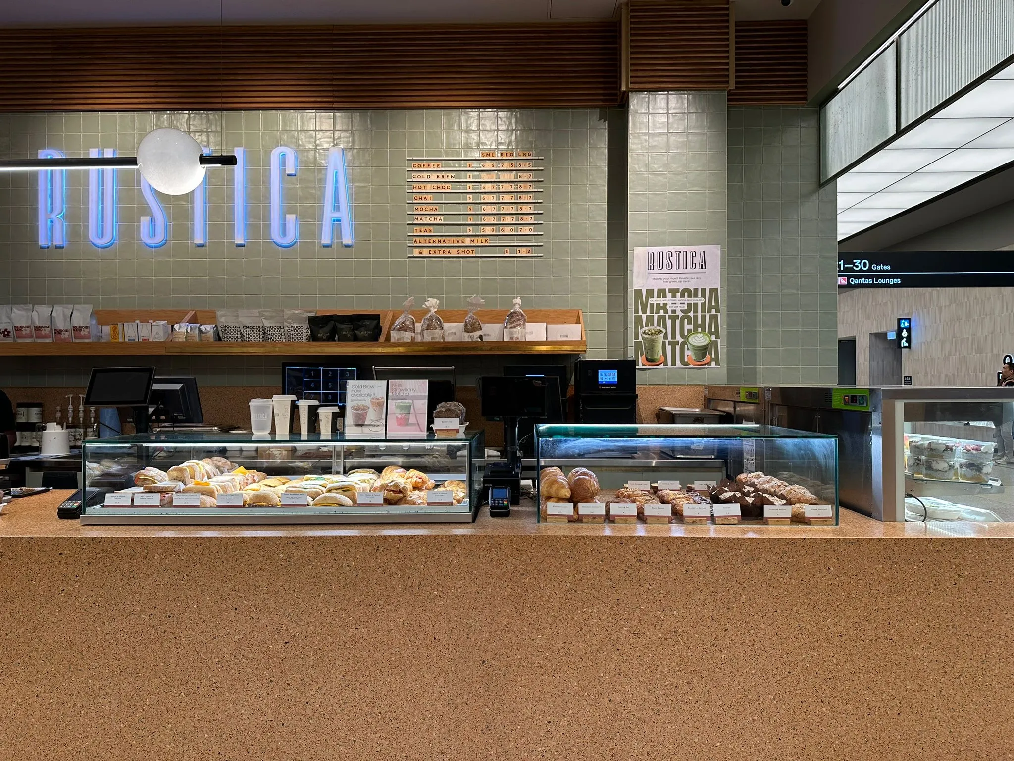 Rustica café counter with baked goods in glass cases and illuminated sign on tiled wall.
