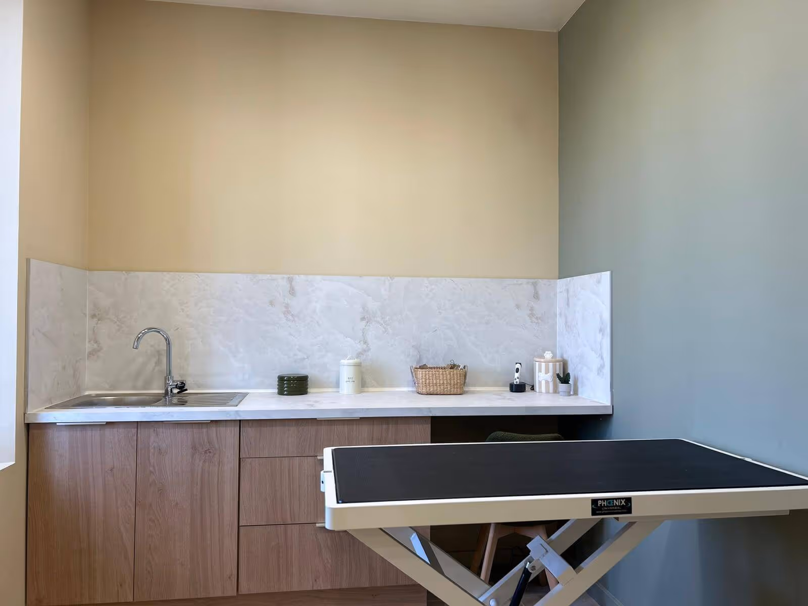 Espace de consultation avec un lavabo, un comptoir en marbre et une table d'examen noire ajustable.