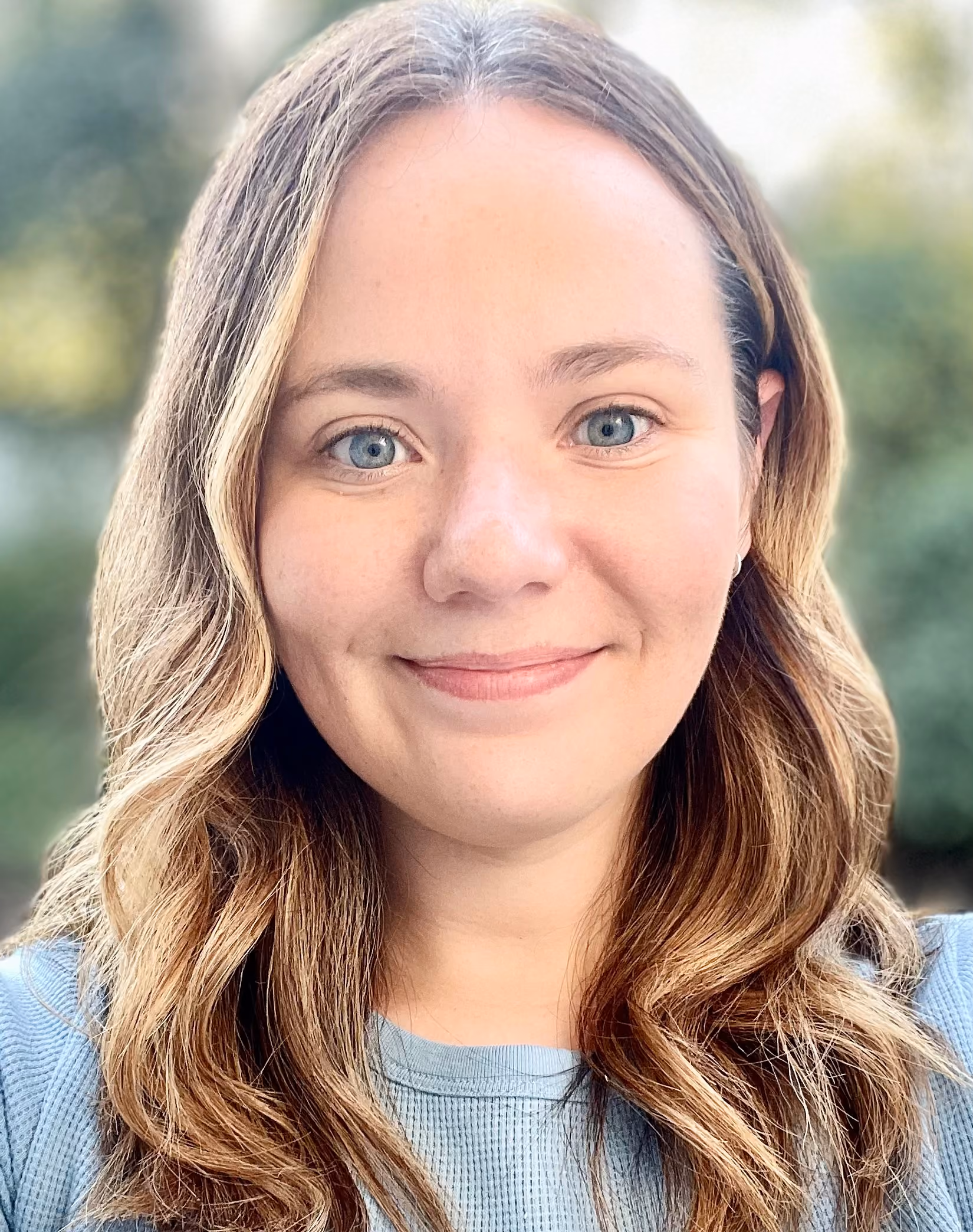 Close-up of a smiling woman with wavy blonde hair and blue eyes wearing a light blue top.
