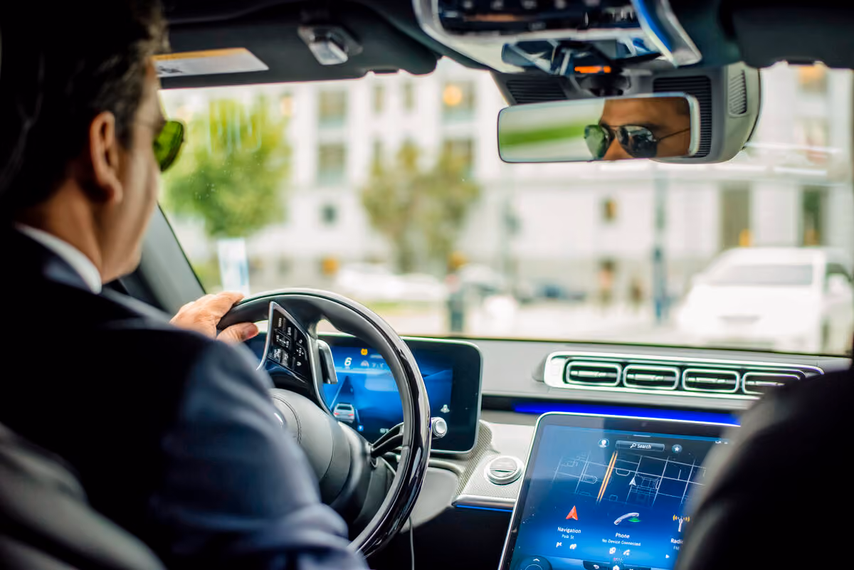 Chauffeur at the wheel of a Mercedes with a navigation screen glowing on the dashboard