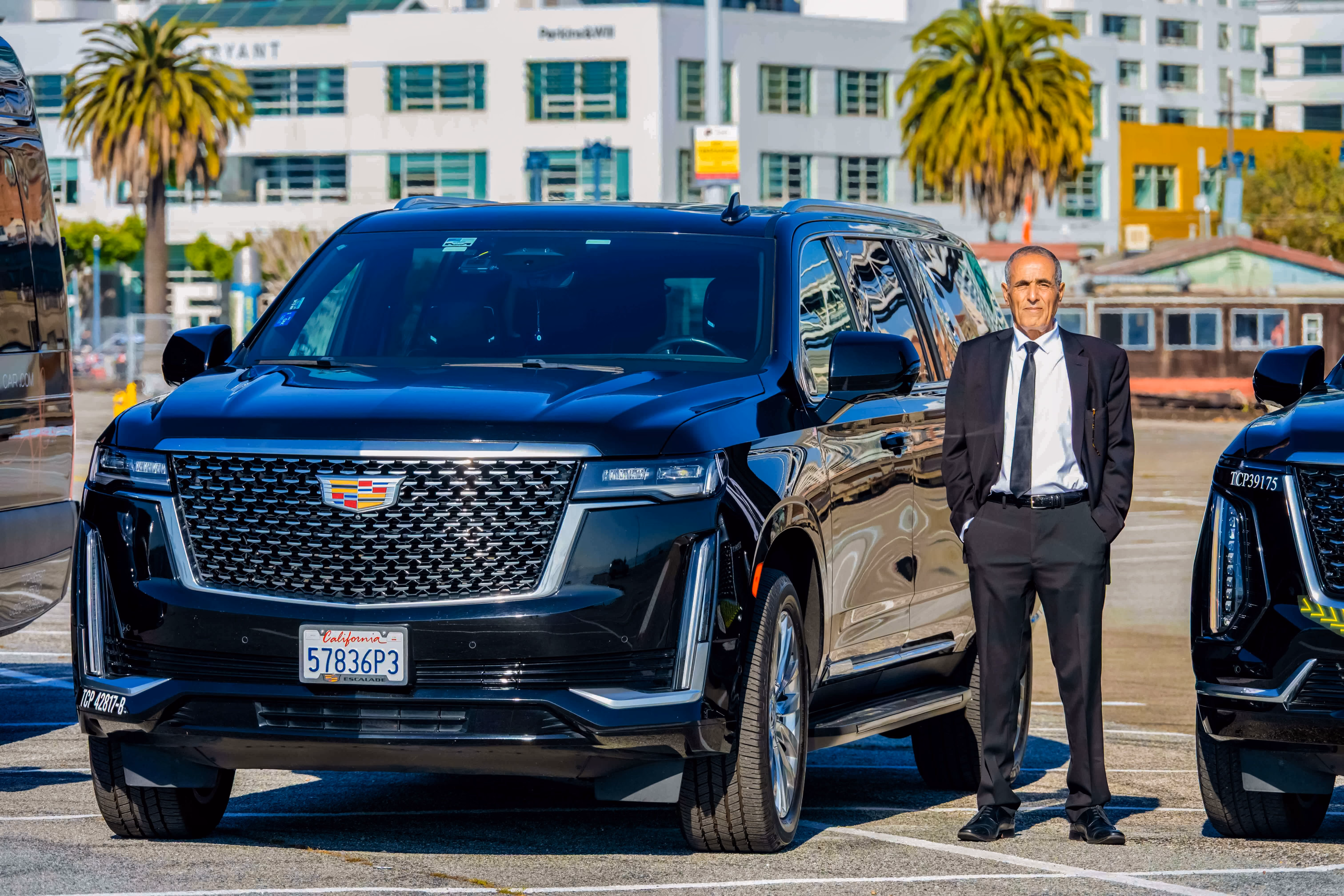 Chauffeur standing at the front of a black Cadillac Escalade in a palm lined parking lot