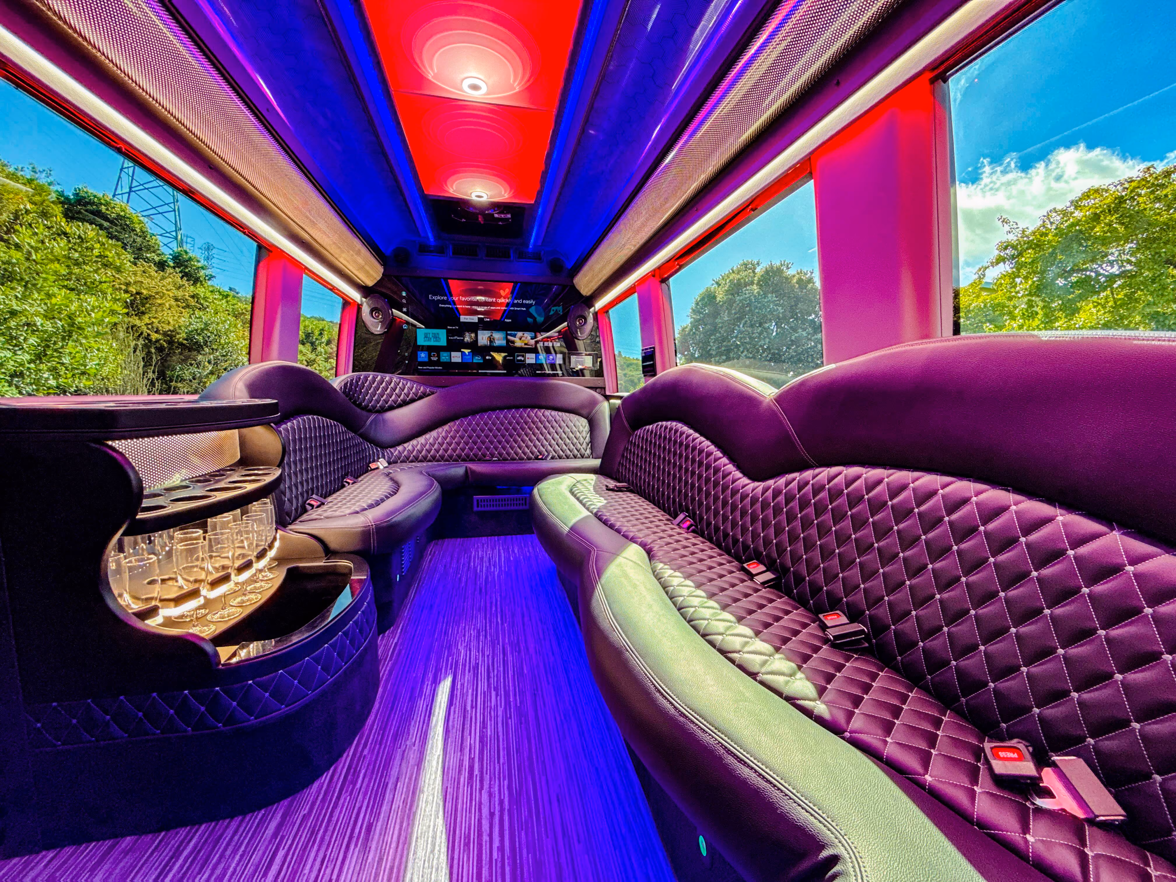 Limo bus interior with purple quilted wraparound seating, a bar console and LED lit ceiling