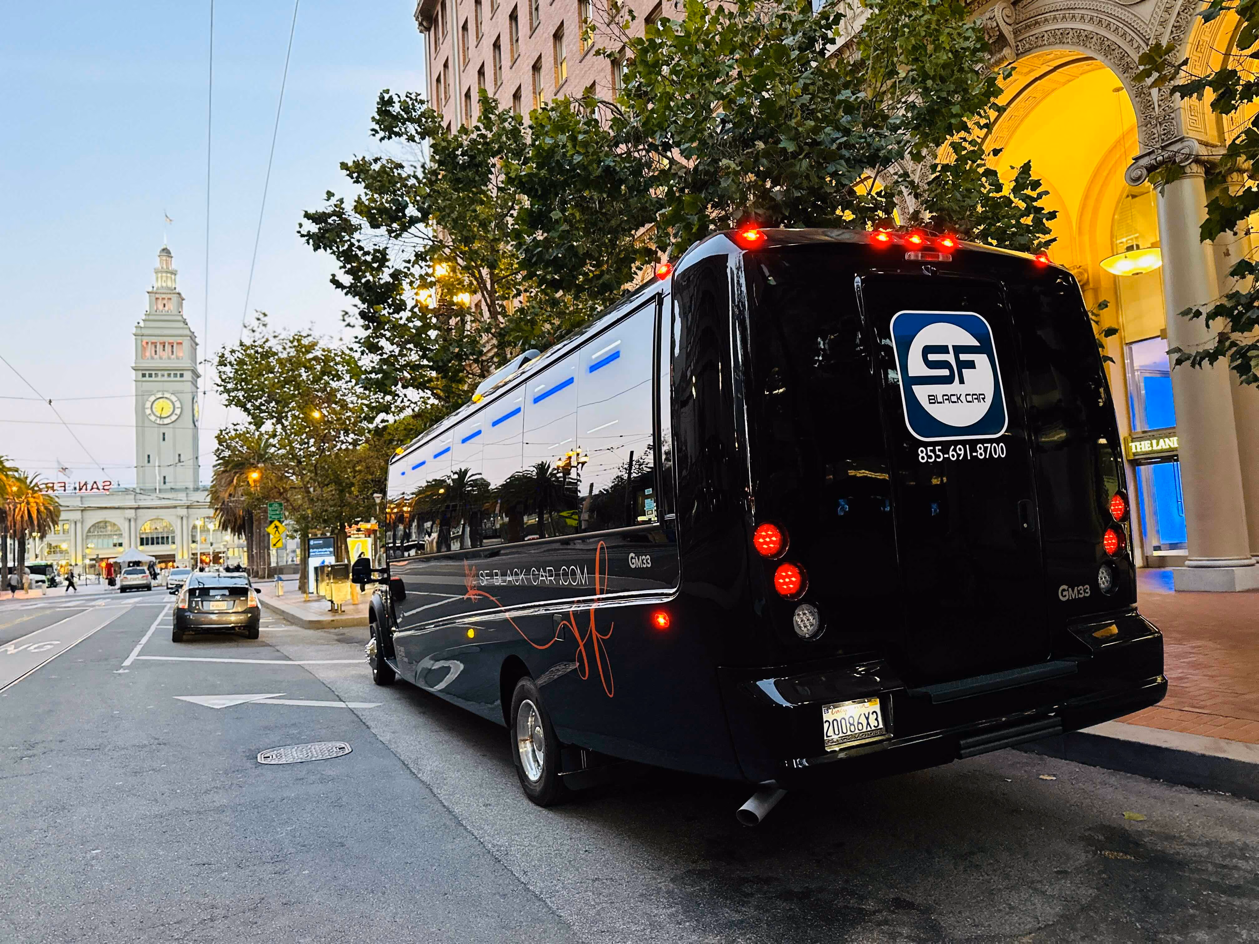 Black SF Black Car mini coach bus on Market Street with the San Francisco Ferry Building clock tower in the background