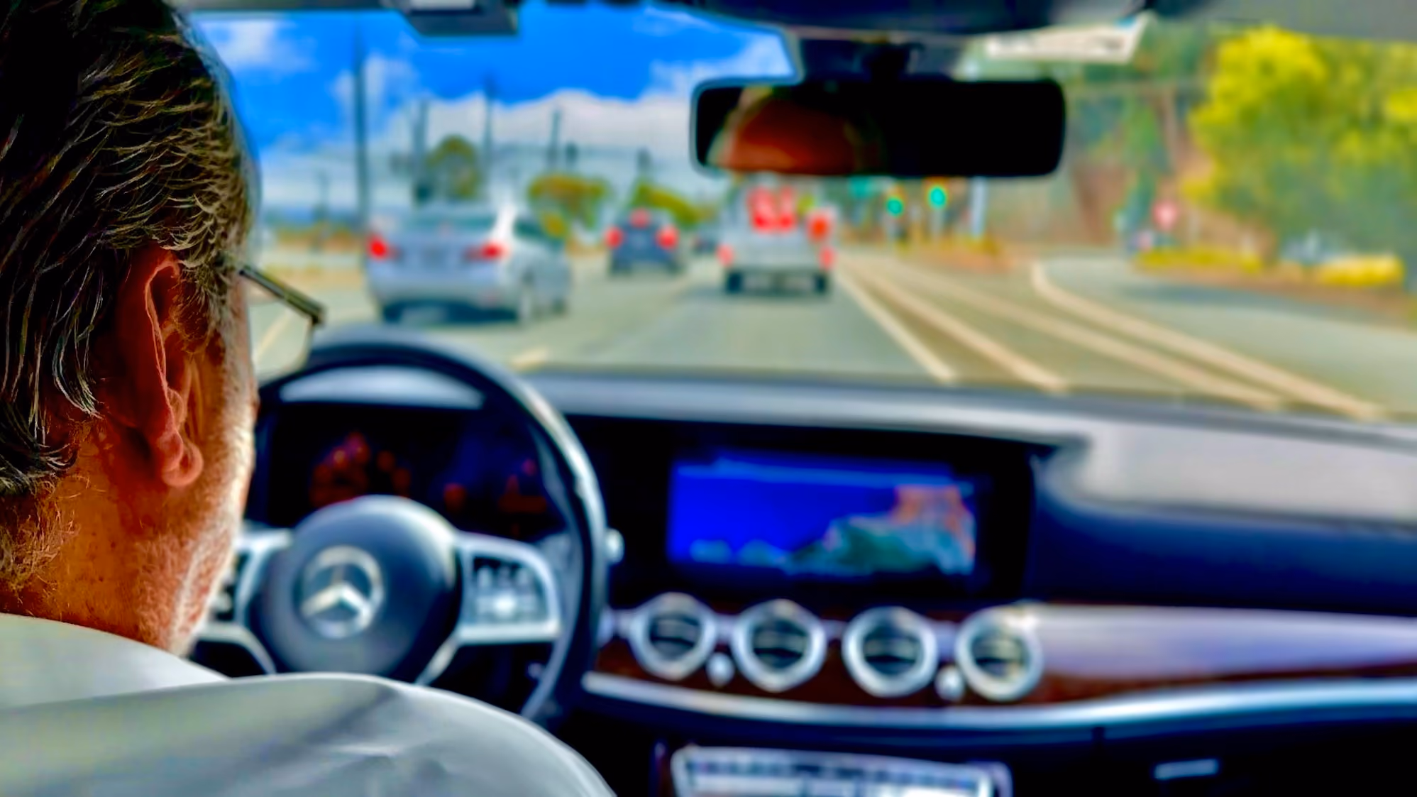 View from inside a Mercedes-Benz sedan of the chauffeur driving through daytime traffic
