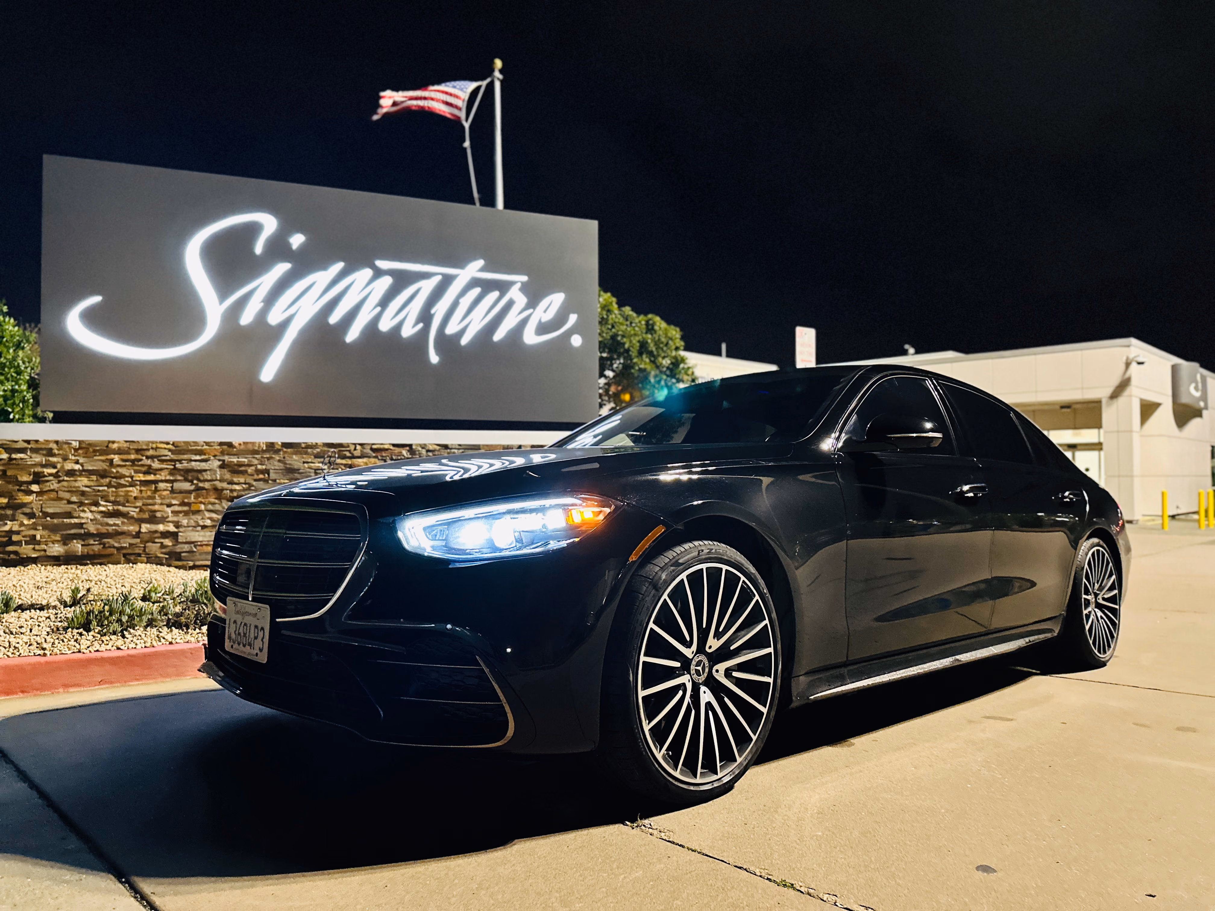 Black Mercedes-Benz S-Class sedan parked at night in front of a Signature sign