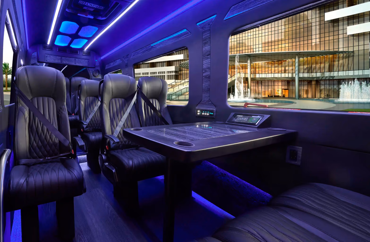 Interior of a luxury Mercedes Sprinter van with black leather seats, a center table, and blue ambient lighting