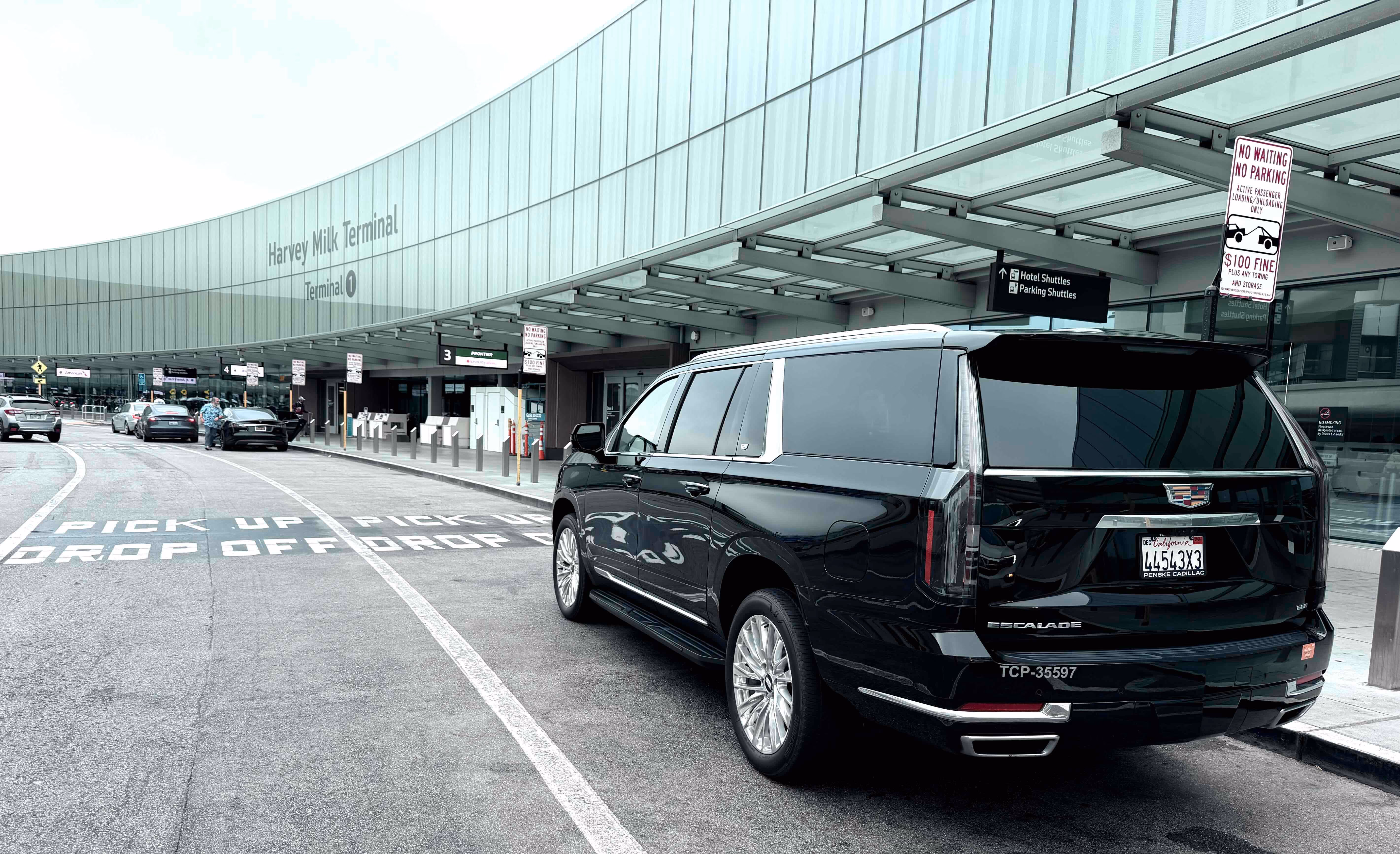 Black Cadillac Escalade at an airport terminal curb marked pick up and drop off