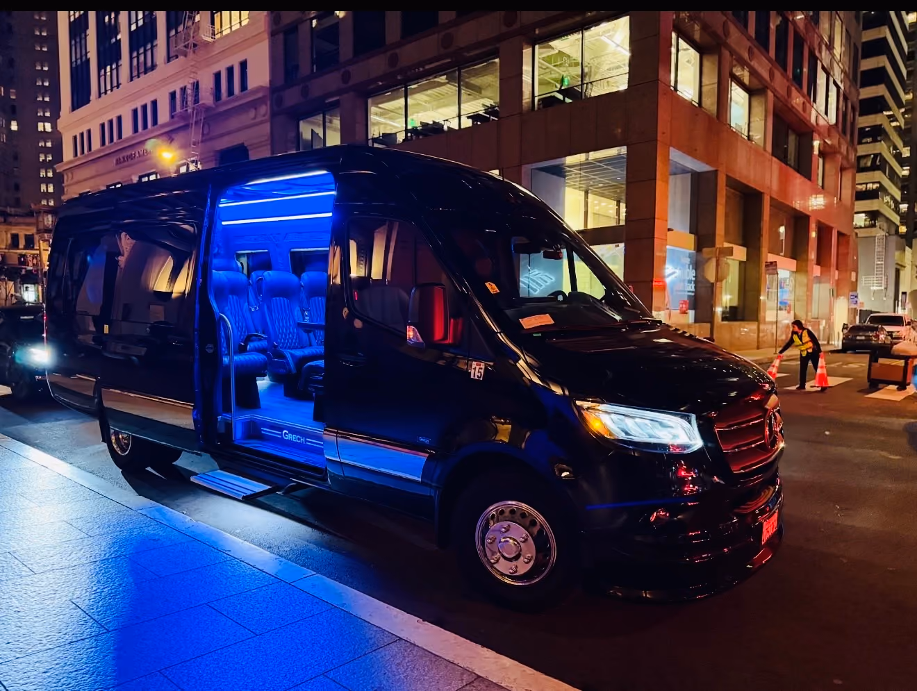 Black Mercedes Sprinter van with open door and blue interior lighting on a city street at night