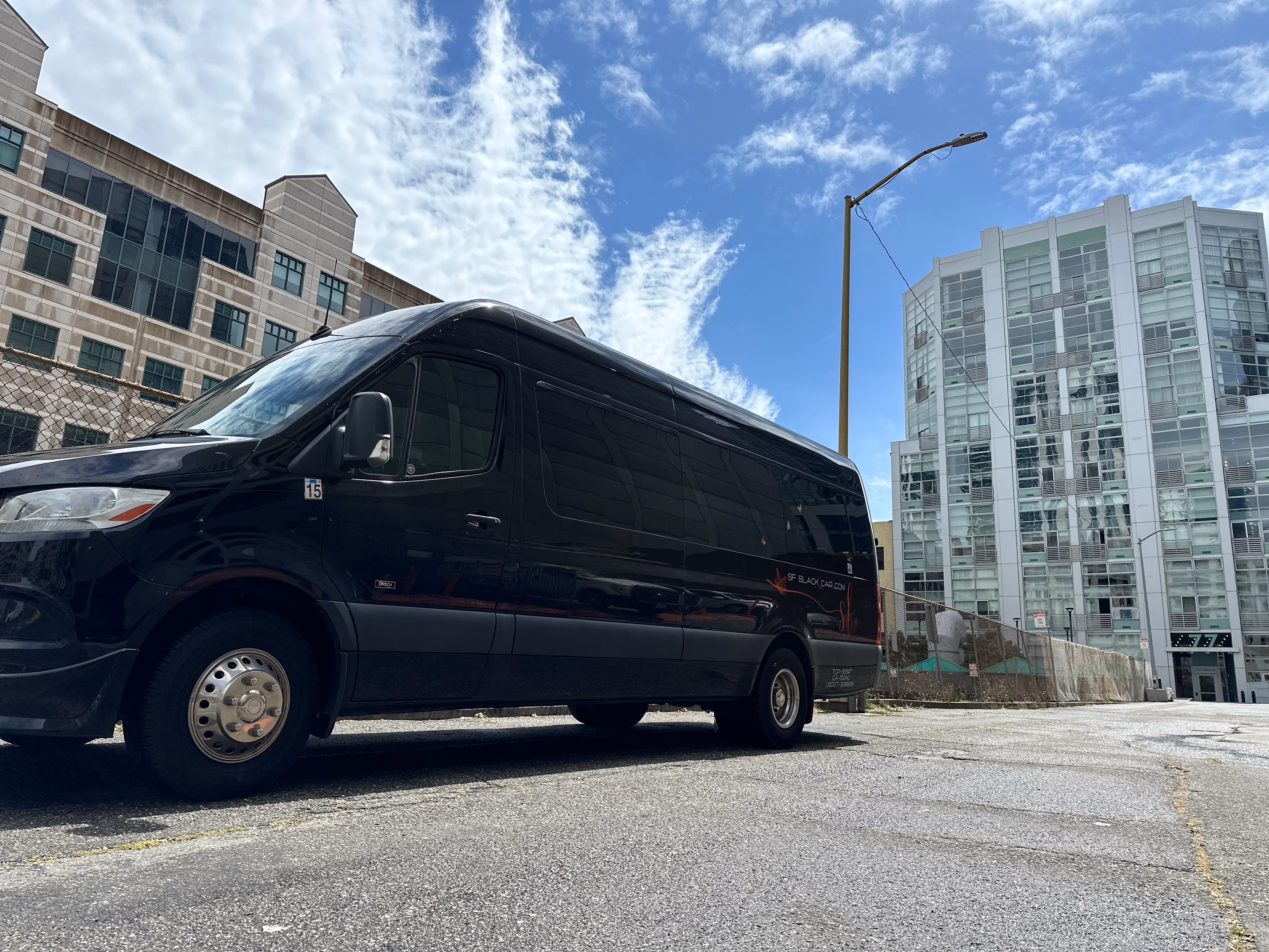 Black van parked on a street beside modern apartment buildings under blue sky