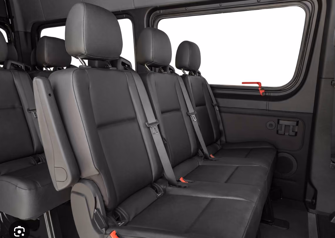 Rows of black leather passenger seats inside a van beside a window