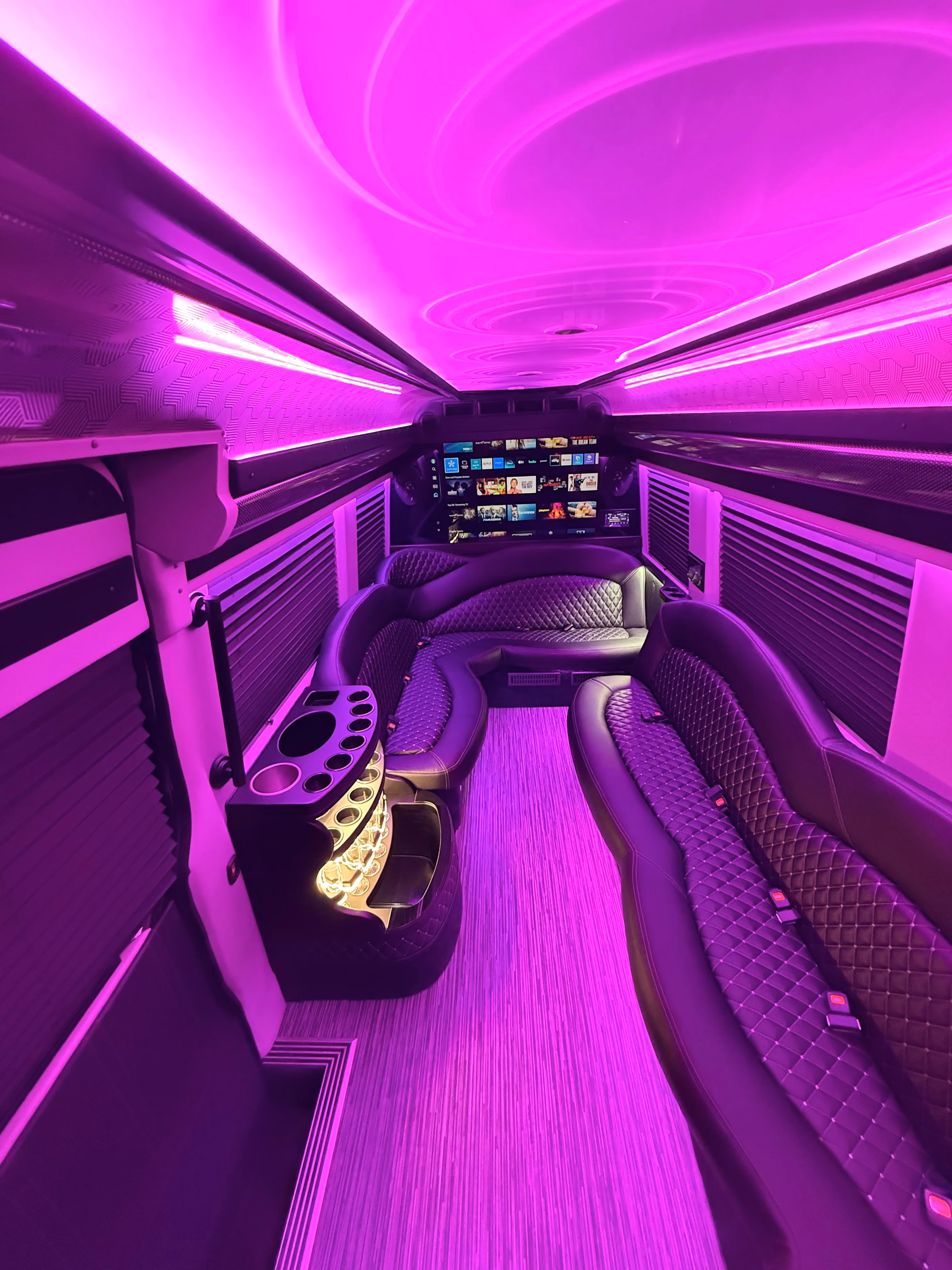 Limo van interior with quilted bench seats under bright pink LED ceiling lighting