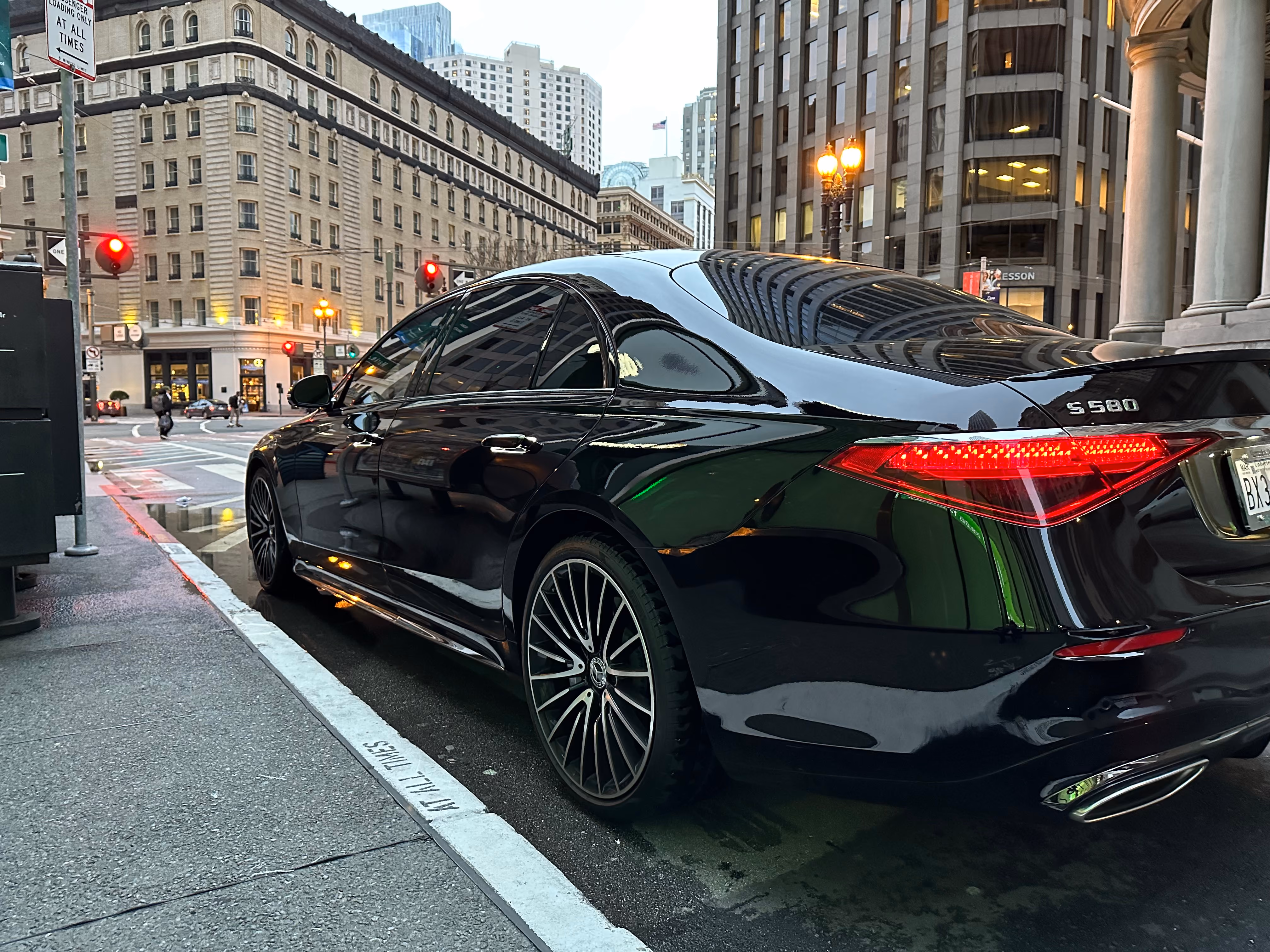 Rear view of a black Mercedes S 580 sedan at a city intersection with stone buildings