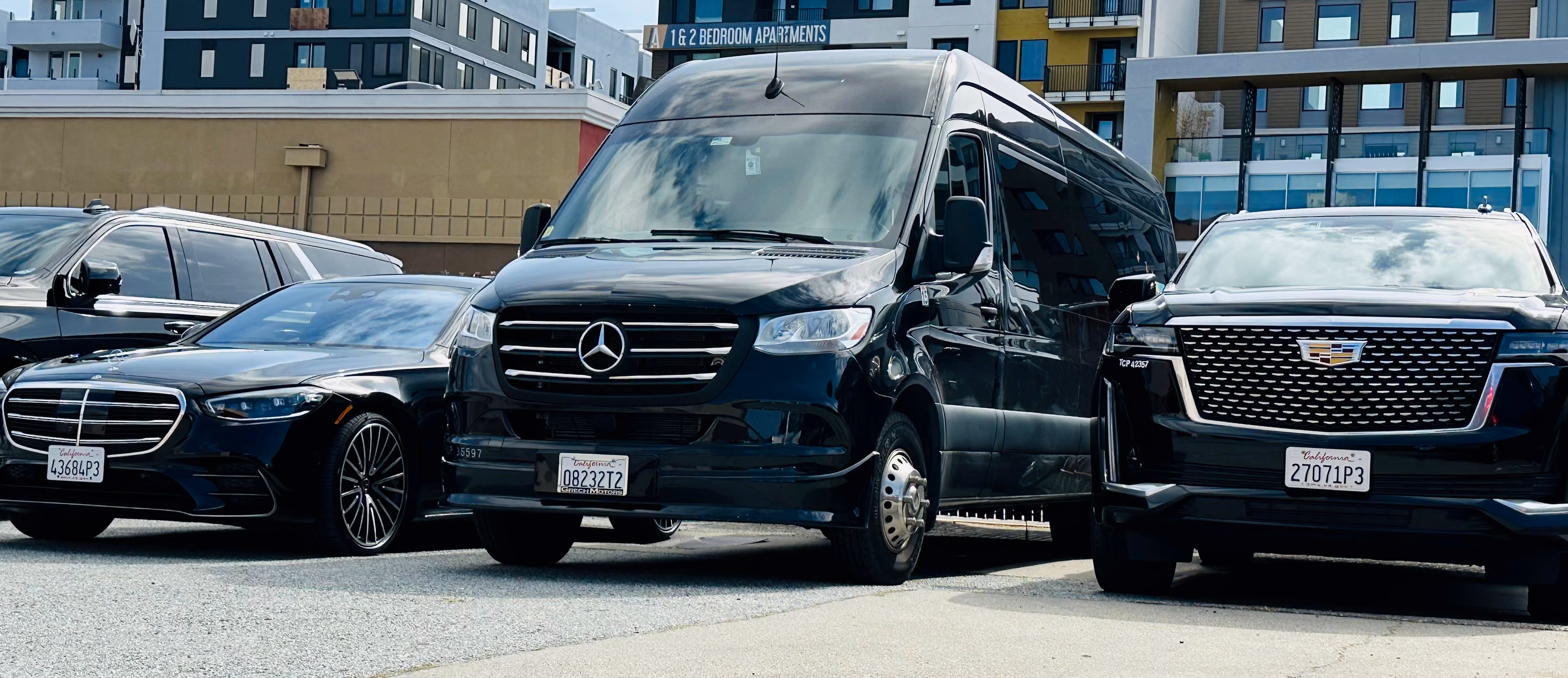 Black Mercedes sedan, Sprinter van and Cadillac SUV parked in a row on a city street