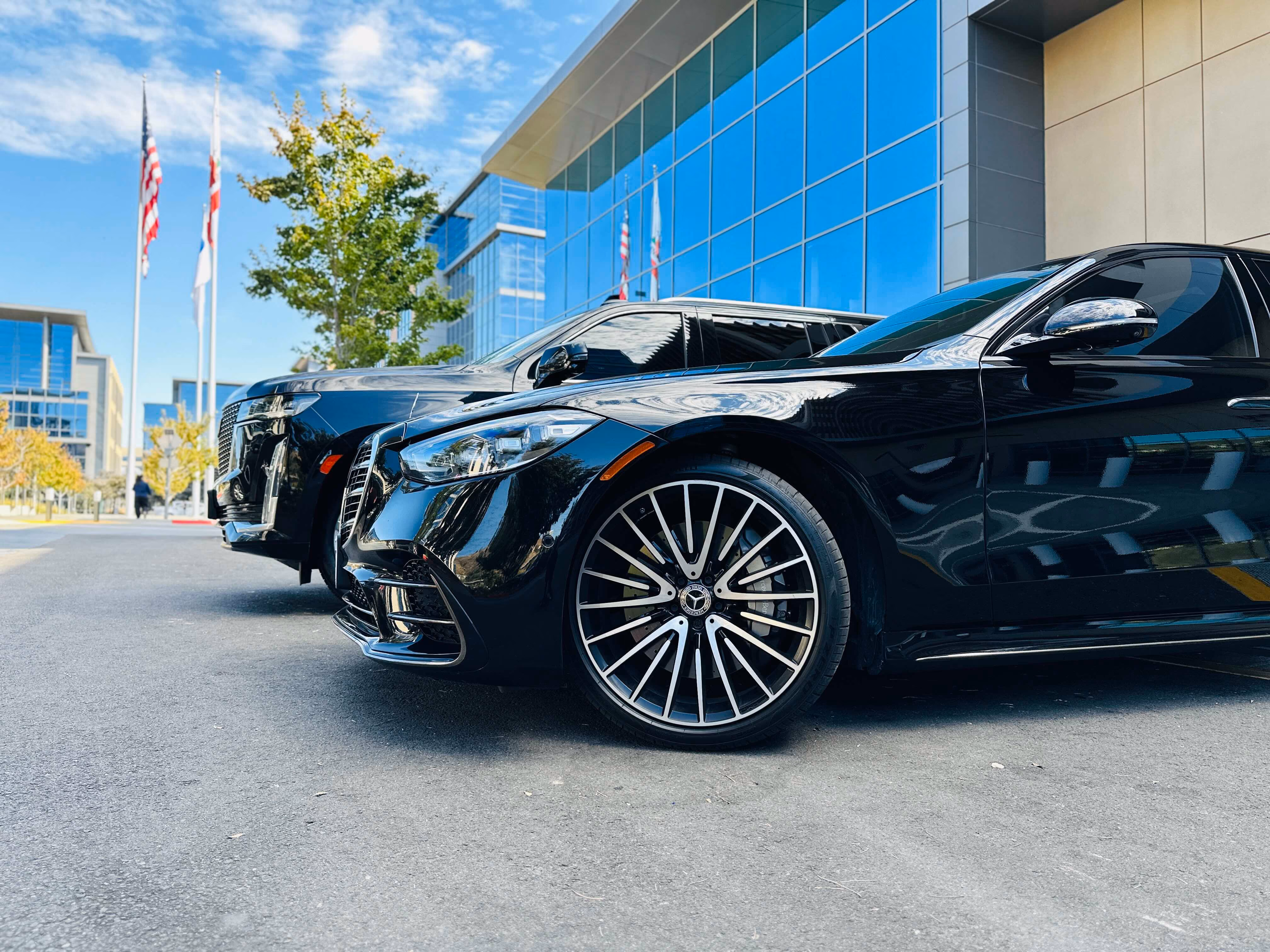 Black Mercedes sedan parked near flagpoles and a blue glass building