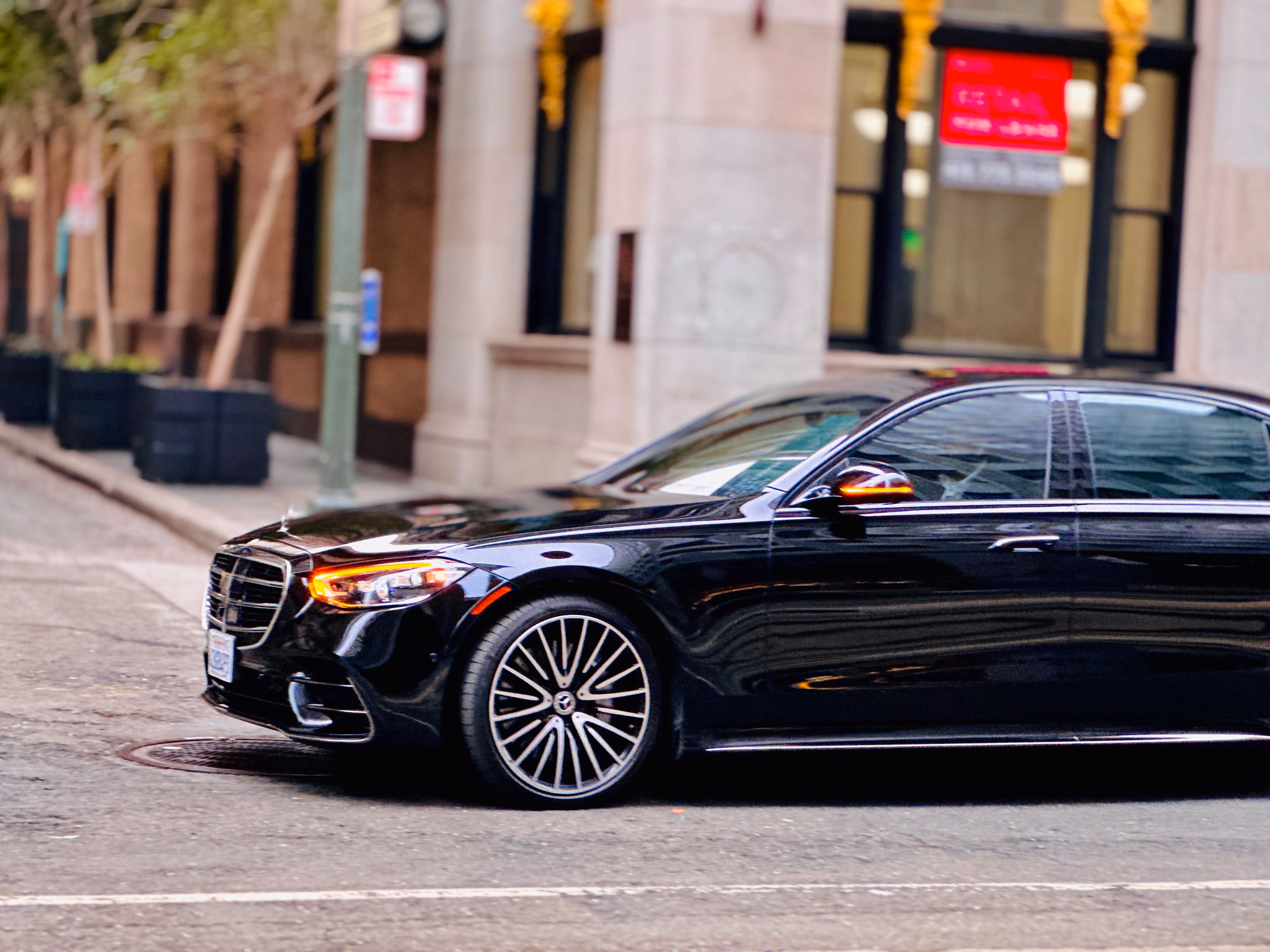 Black Mercedes sedan parked on a city street beside a stone building