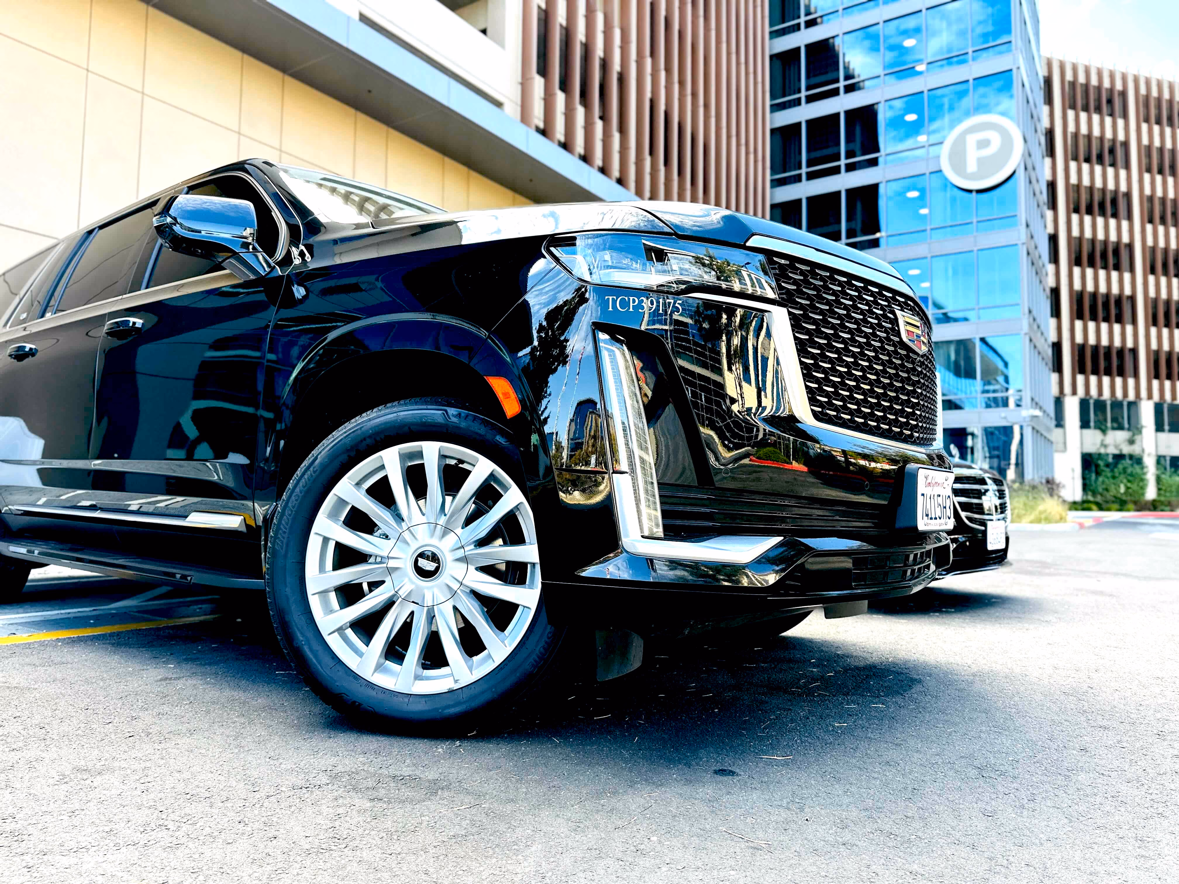 Black Cadillac Escalade with chrome grille parked on a city street beside office towers