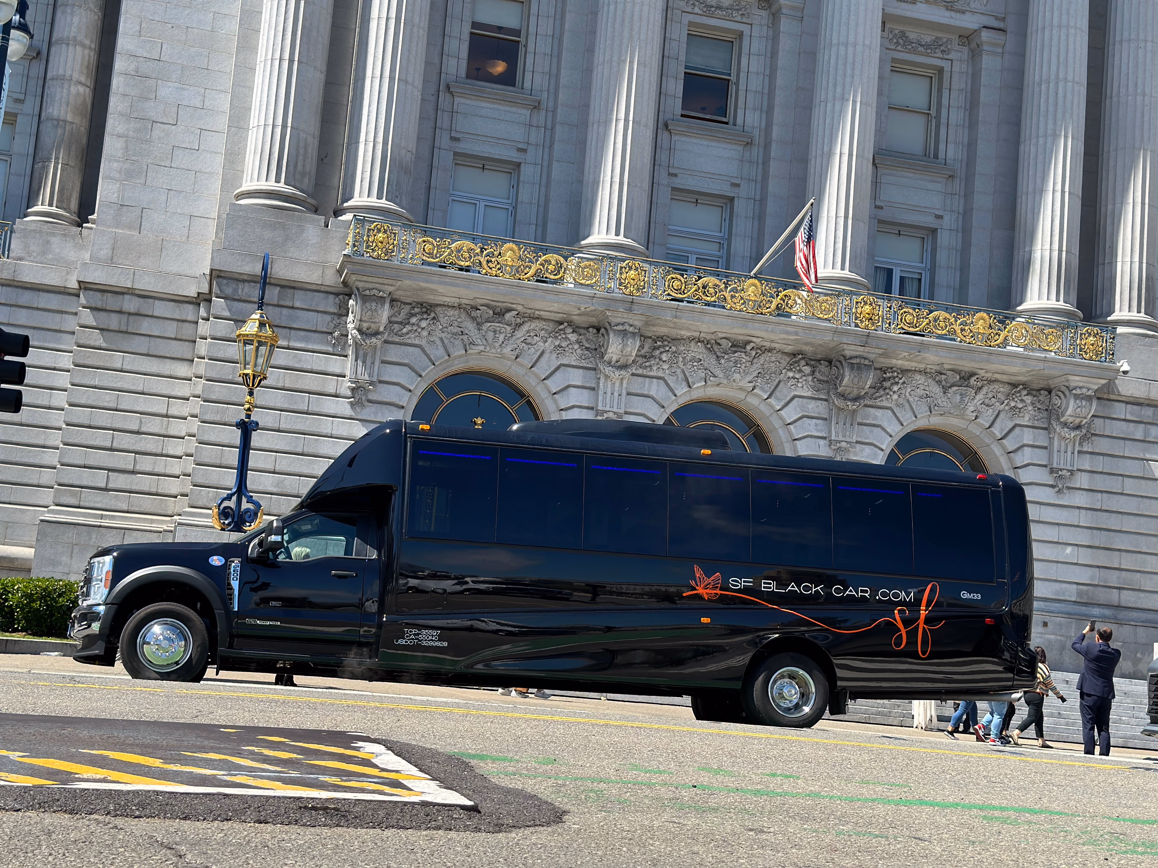 Black passenger shuttle bus with SF Black Car branding parked in front of a stone building with columns.