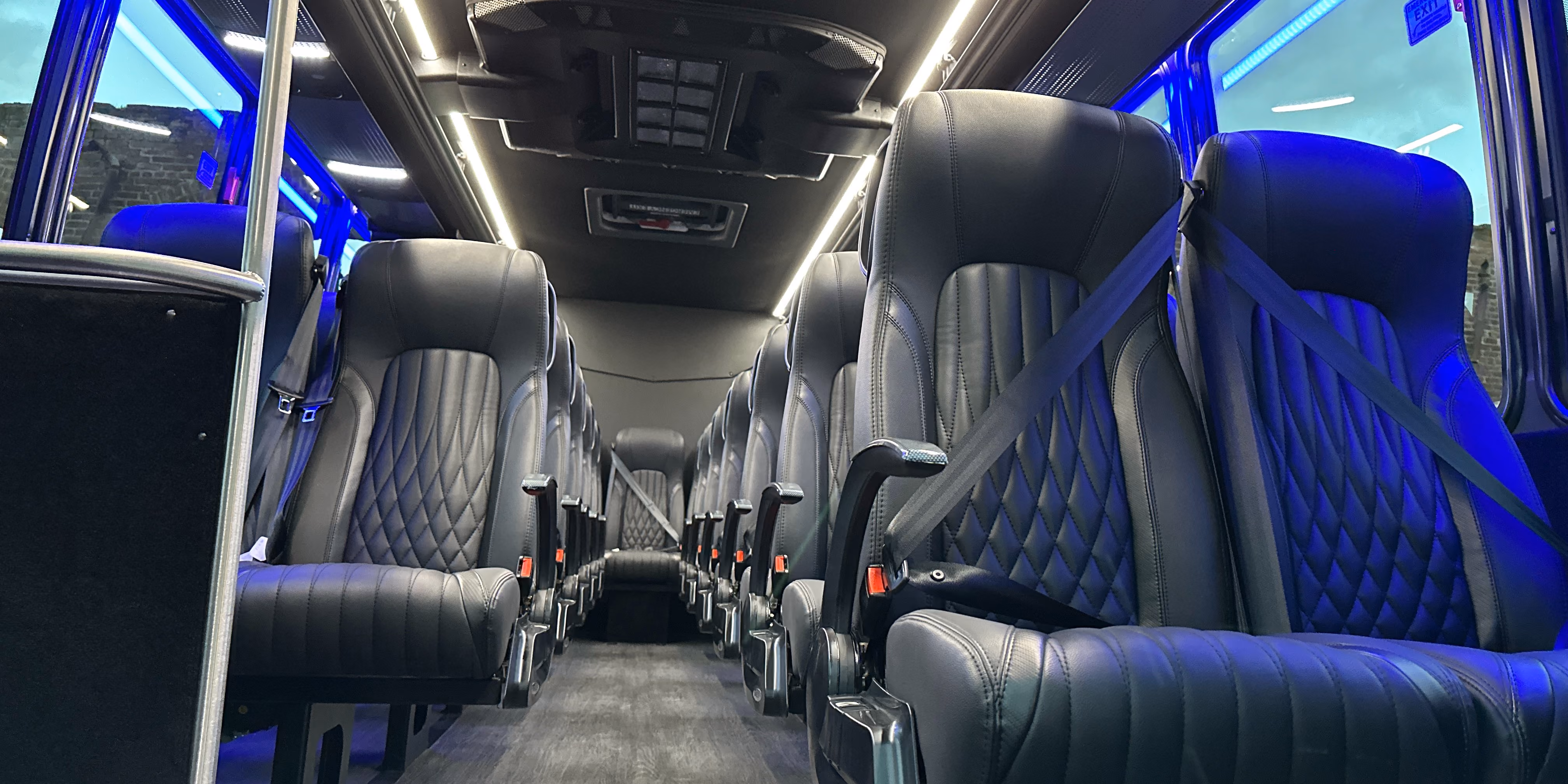 Interior of a modern coach with rows of black leather seats with seatbelts and blue ambient lighting.