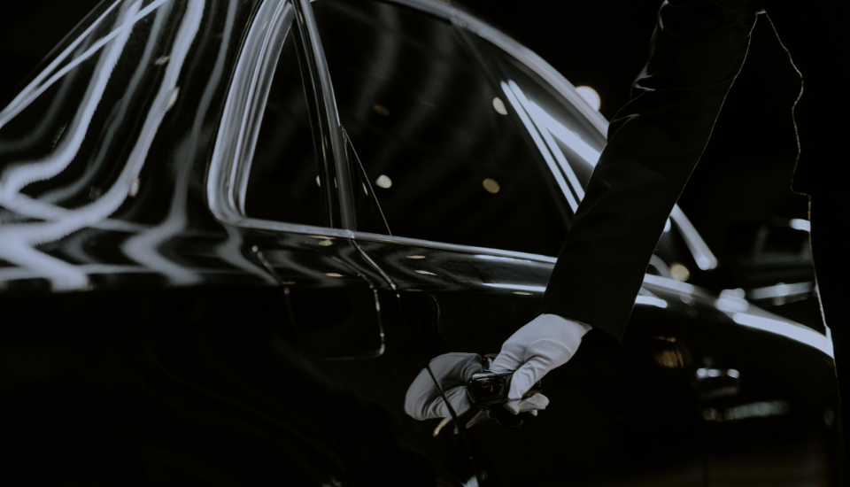 Chauffeur mit weißen Handschuhen öffnet die Tür einer schwarzen Limousine