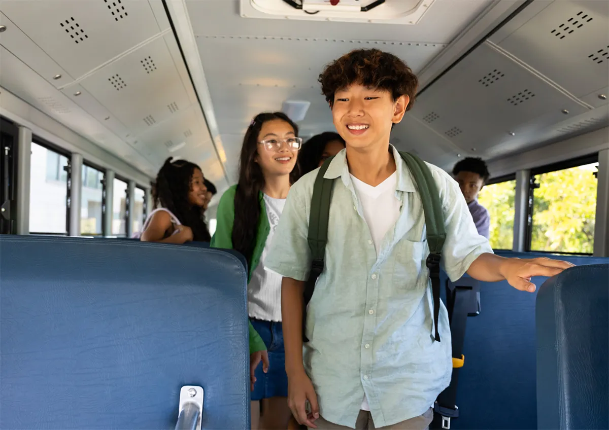Students boarding a school bus, smiling, with backpacks and a diverse group present inside.