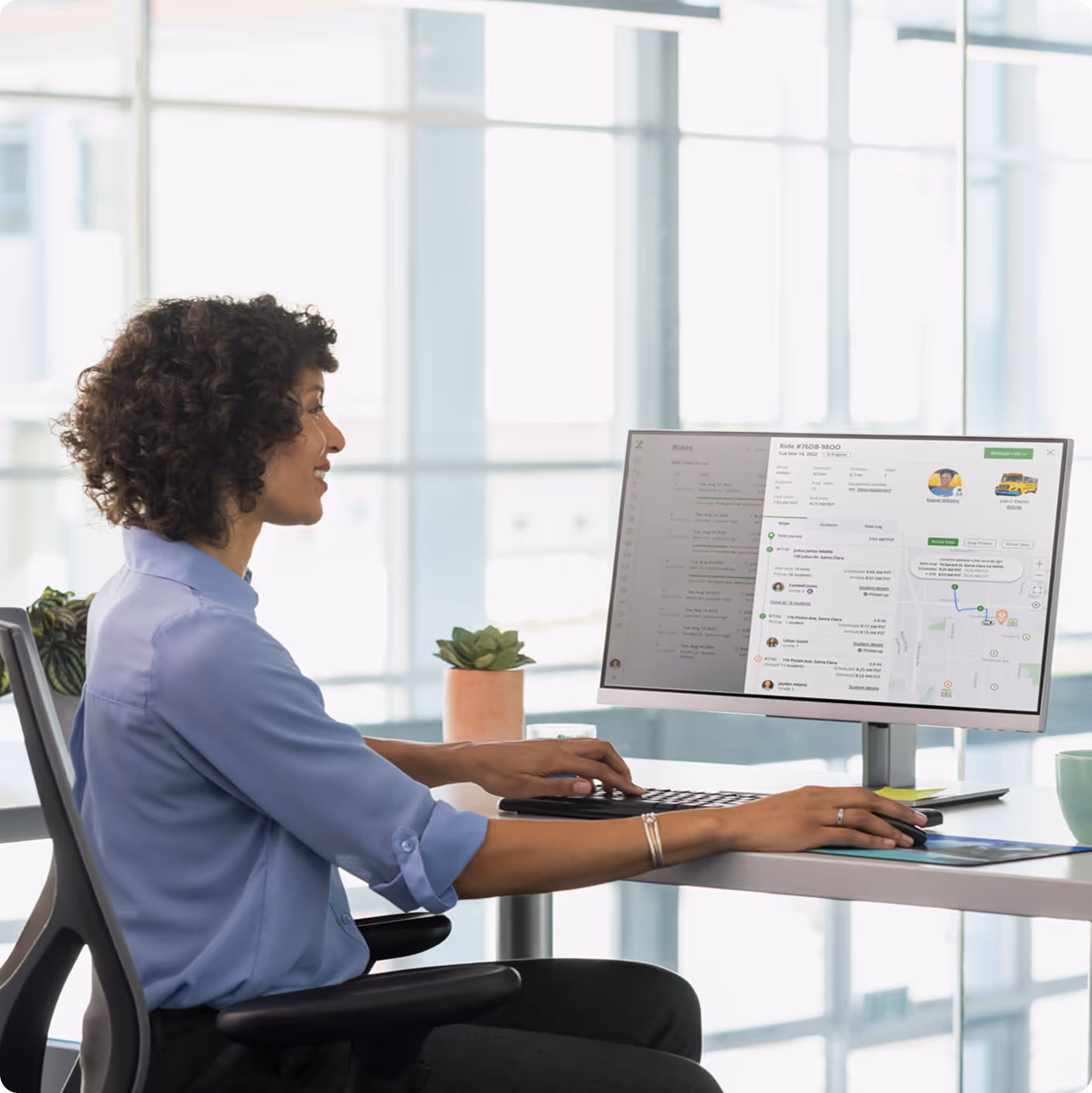 Woman working at a desk with a computer displaying a transportation management dashboard.