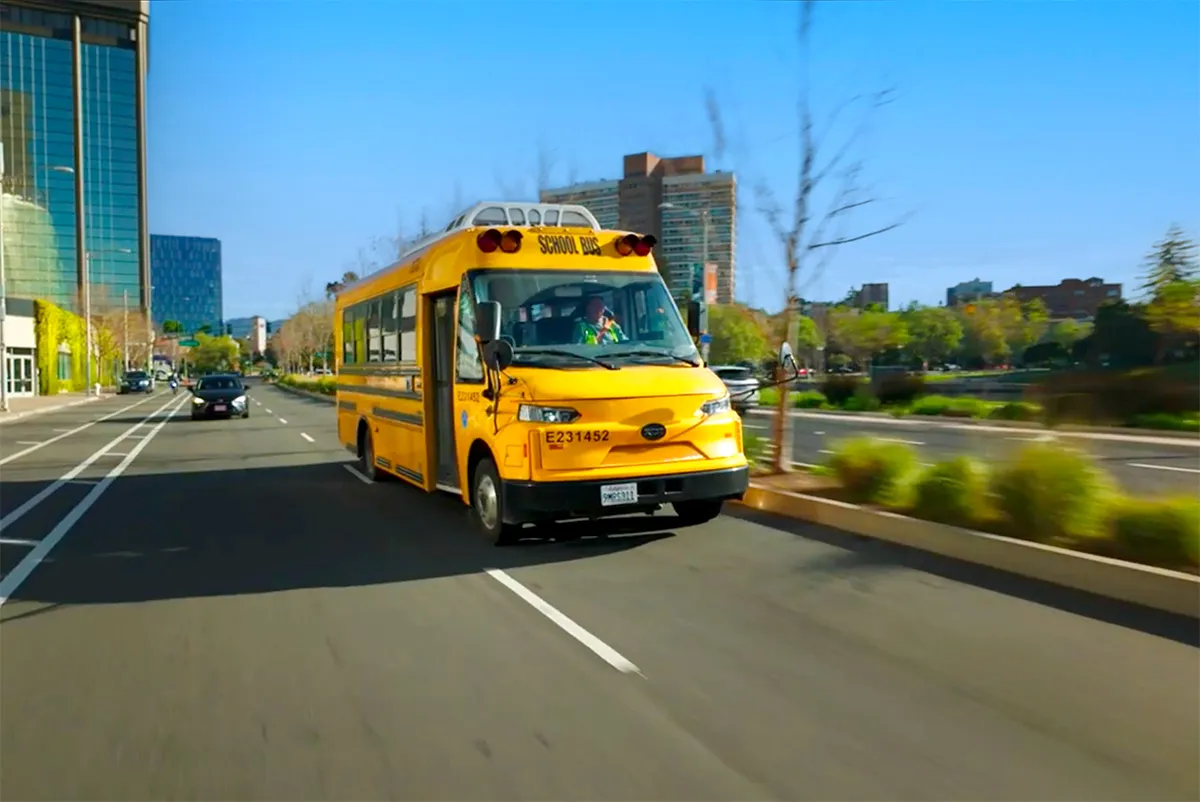 A Zum Services, Inc. school bus driving down a city street lined with high-rise buildings.
