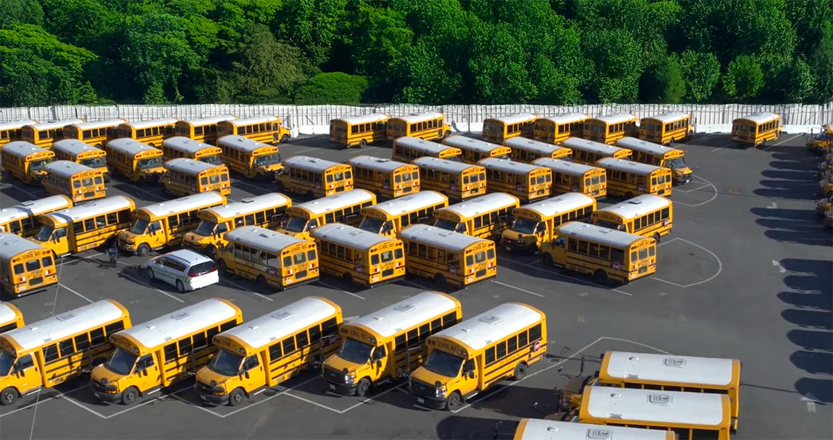 Aerial view of rows of Zum Services, Inc. school buses parked in a fleet yard surrounded by trees.