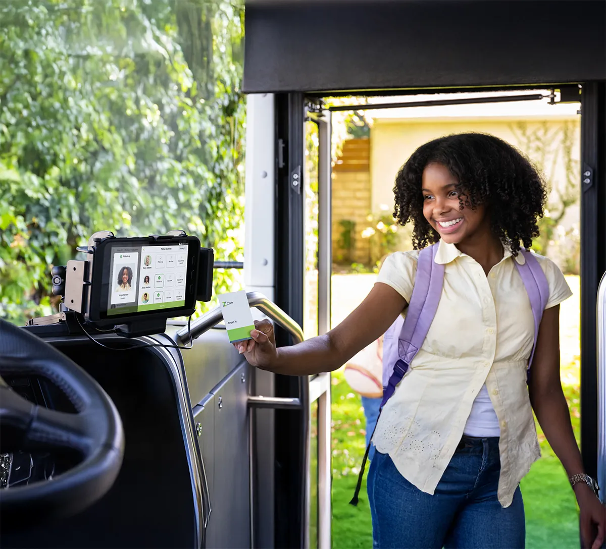 A smiling student scanning her ID card on a Zum Services, Inc. bus tablet as she boards.