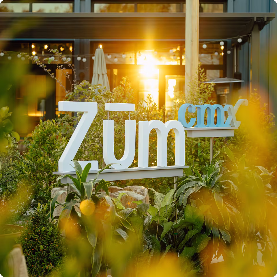 Zum CMX sign amidst greenery with sun setting in the background.