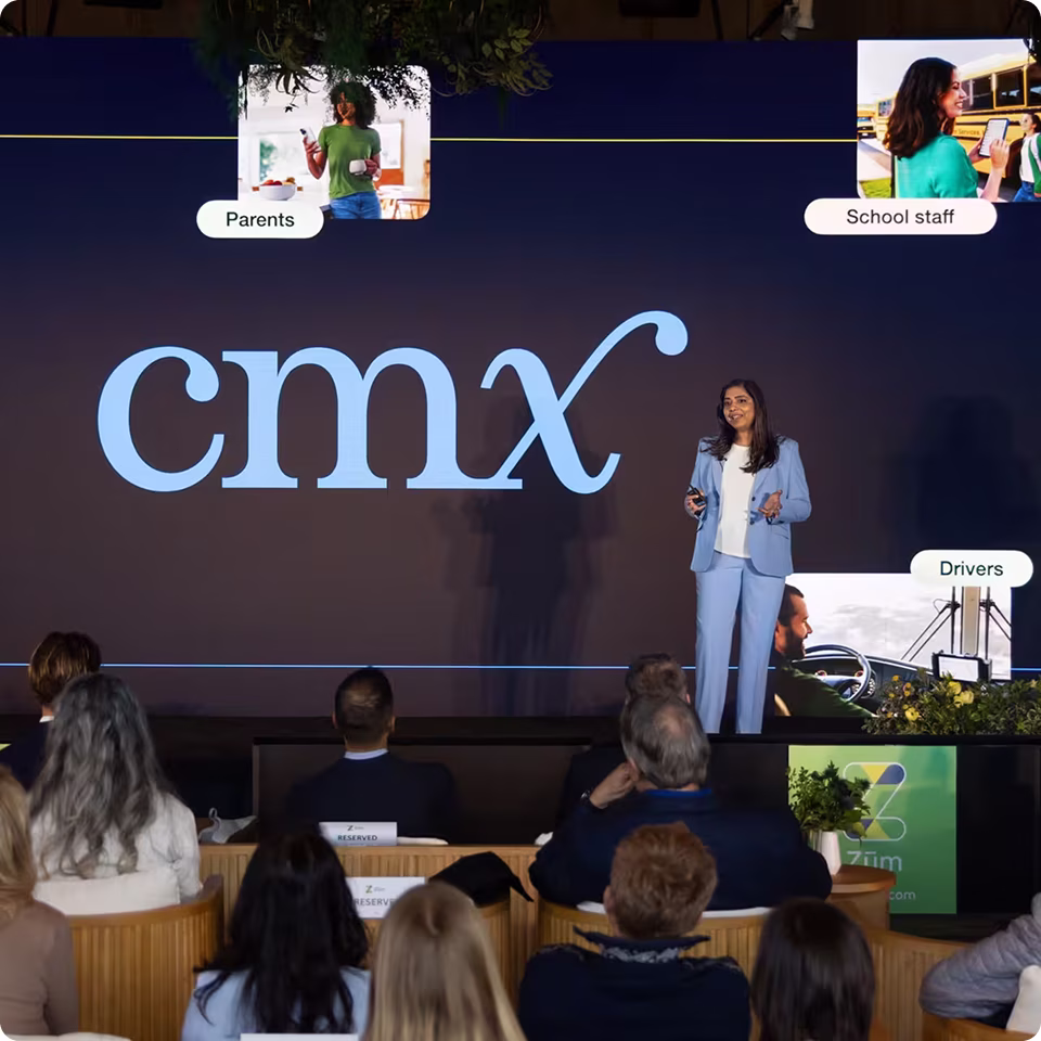 A presenter discusses Zum CMX on stage with audience members seated, featuring a branded backdrop.