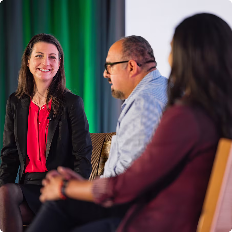 Two speakers engaged in discussion on stage, with a woman in a blazer and a man in a checked shirt.