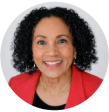 Smiling woman with curly hair, wearing a red blazer and a gold necklace, against a light background.