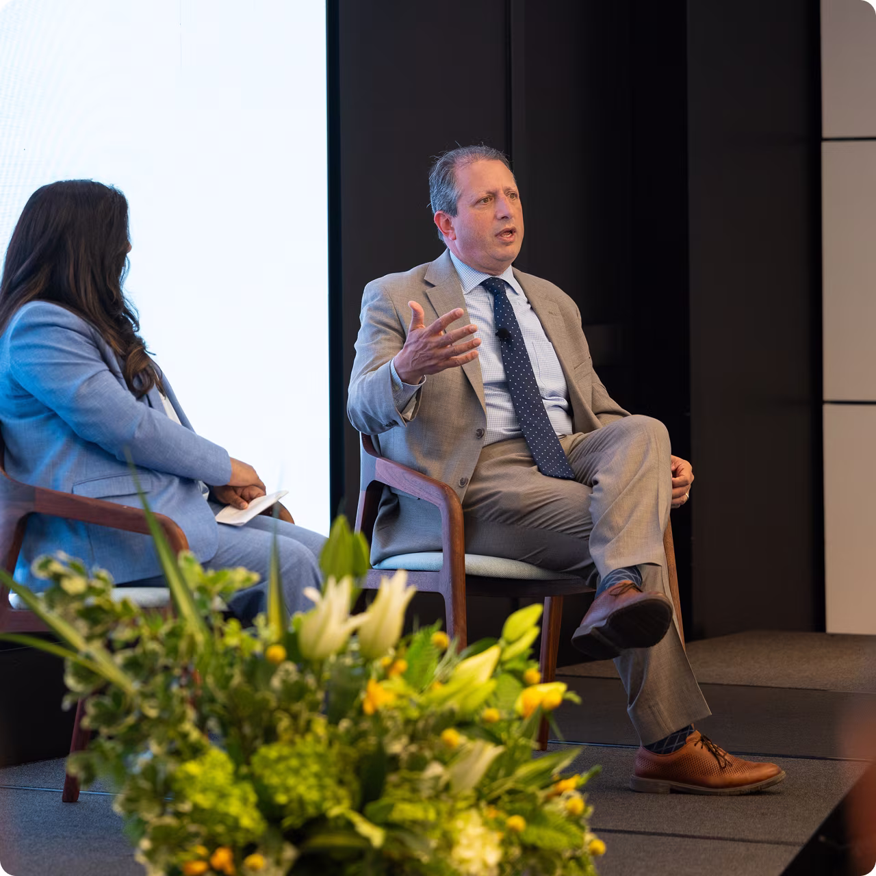Panel discussion with two professionals; one speaking while seated, flowers in foreground.